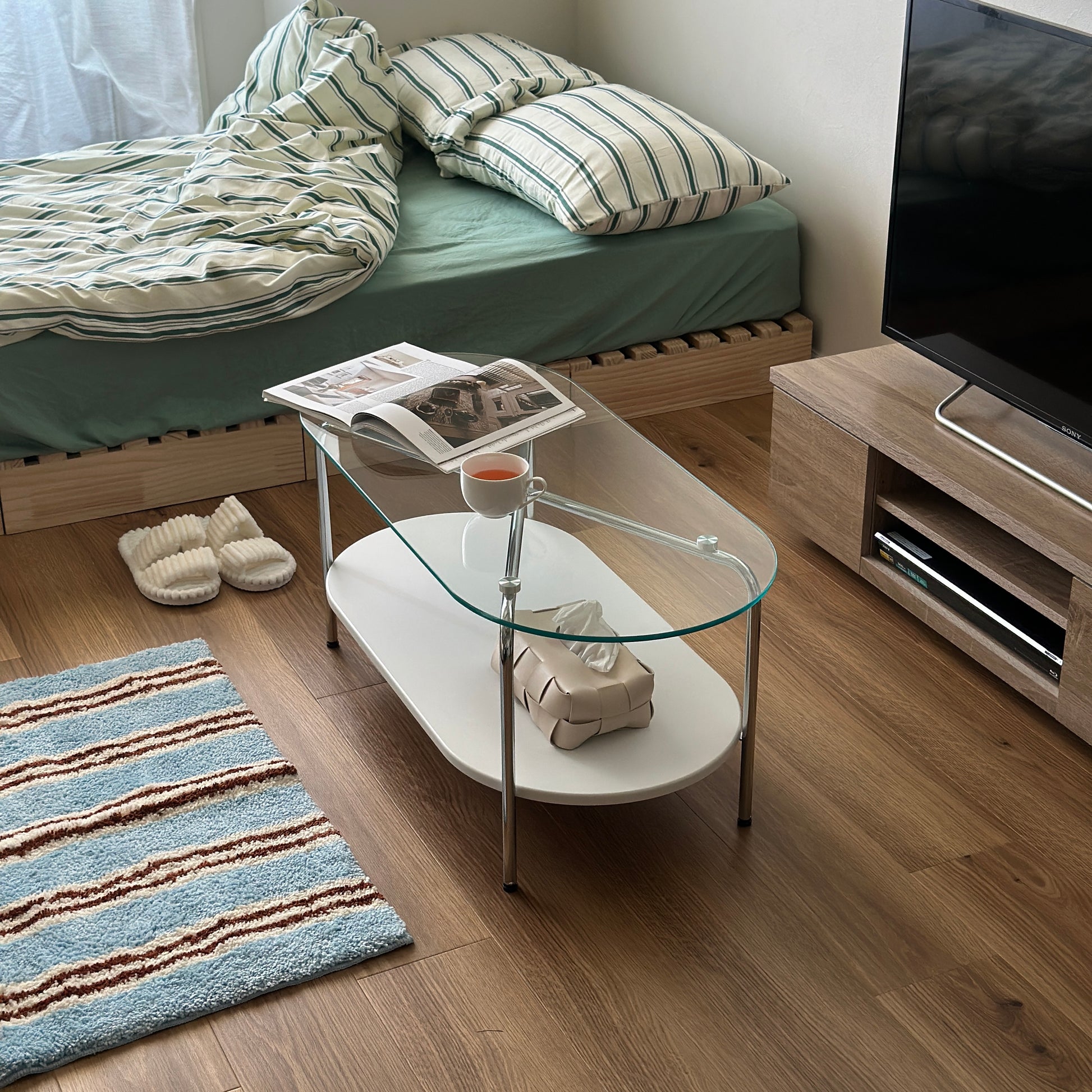 丸みのあるガラス天板のローテーブルの天板上にはコップと雑誌が置かれており、下の棚にはティッシュケースが置かれてある