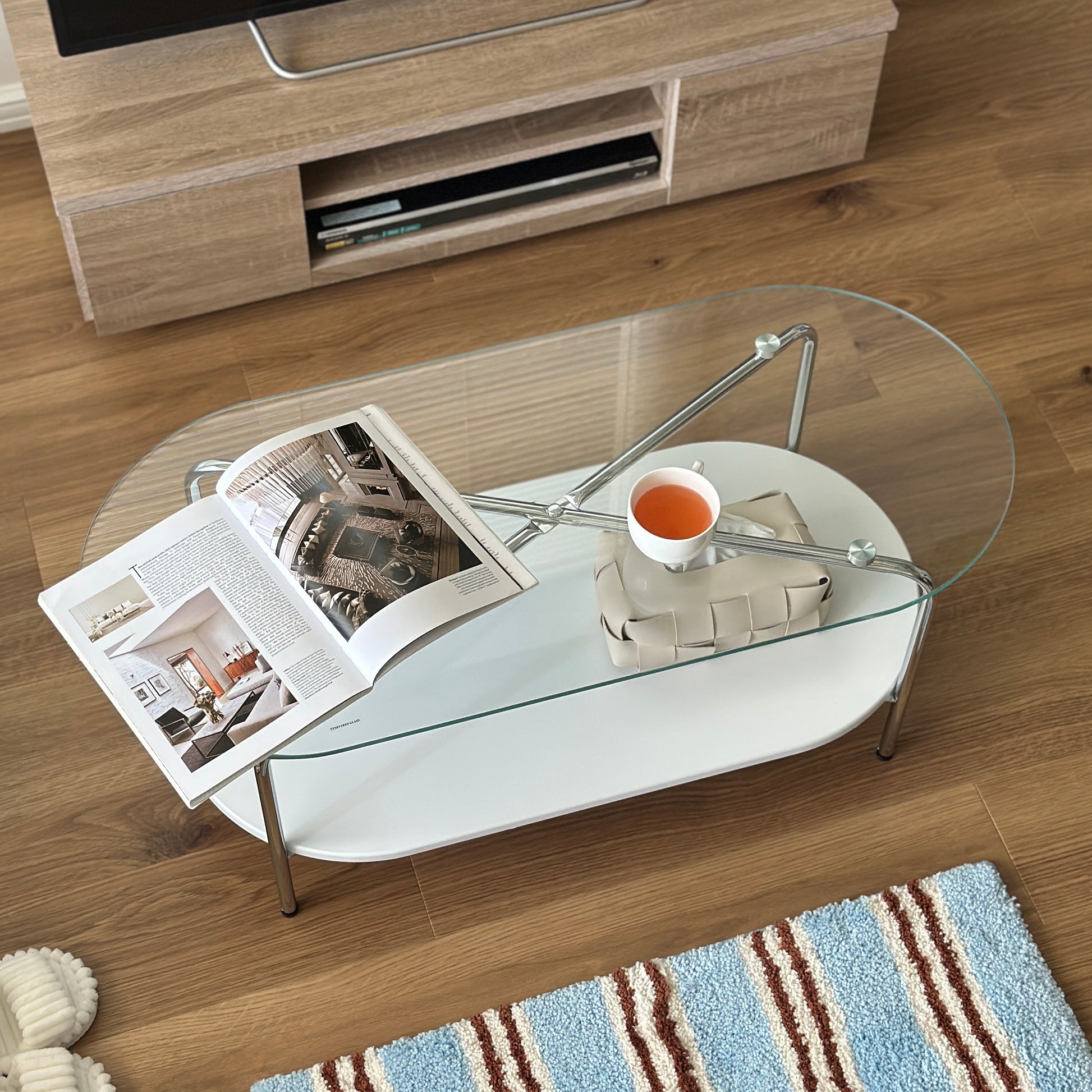 丸みのあるガラス天板のローテーブルの天板上にはコップと雑誌が置かれており、下の棚にはティッシュケースが置かれてある