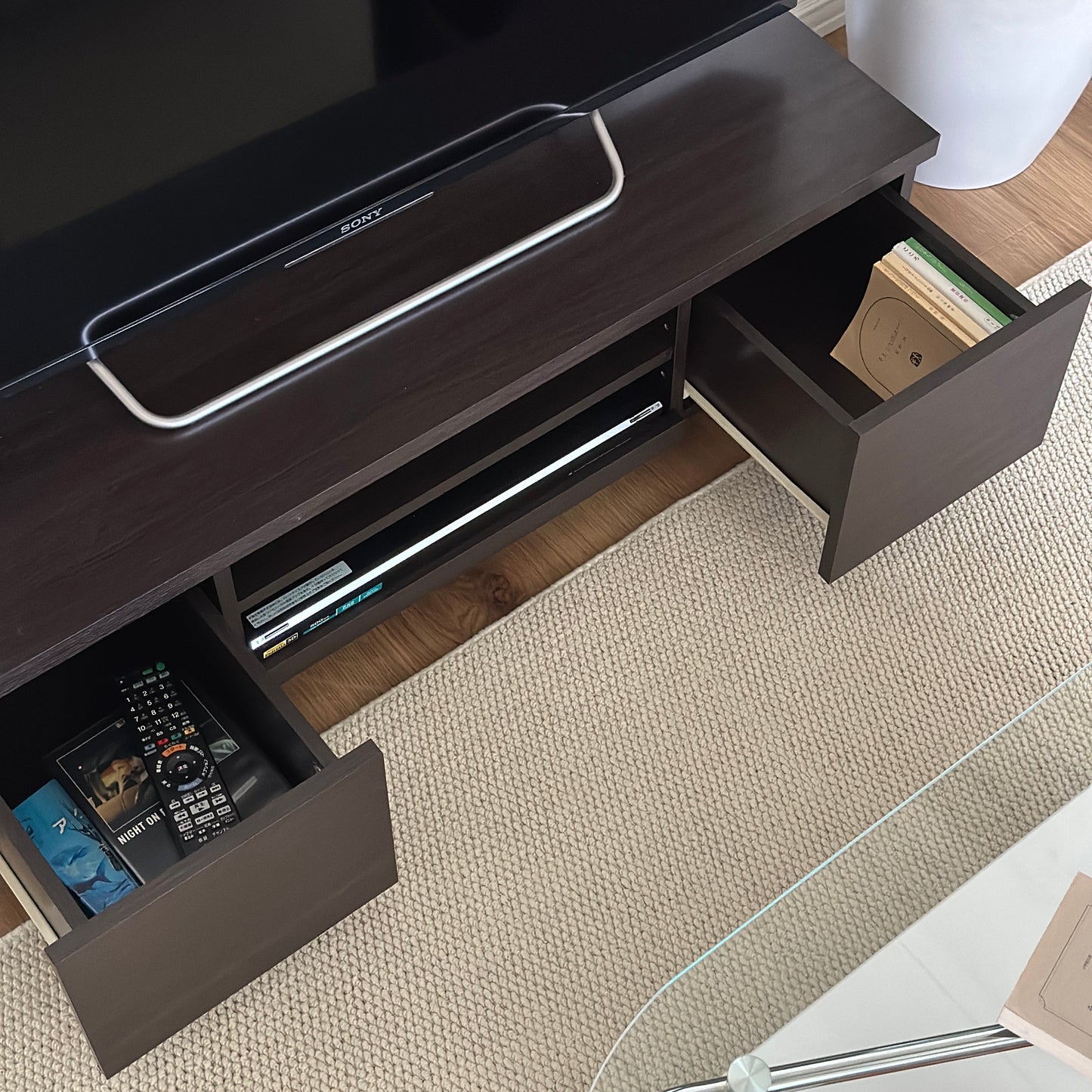 ダークブラウンのテレビボードの引き出し収納に文庫本やテレビのリモコン、DVDが入れられている