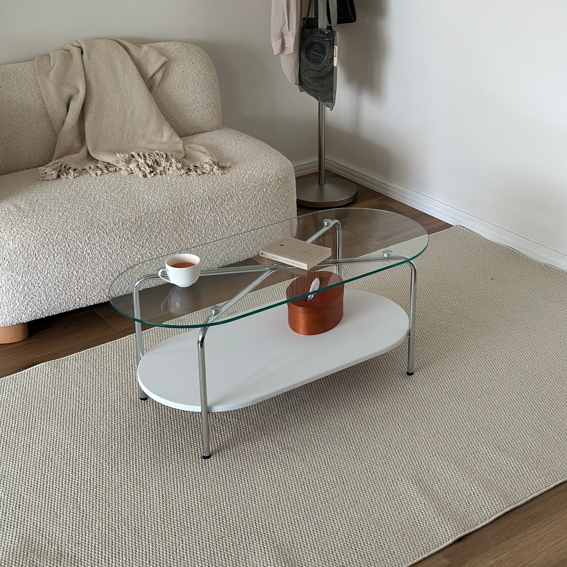 丸みのあるガラス天板のローテーブルの天板上にはコップと文庫本が置かれており、下の棚にはティッシュケースが置かれてある