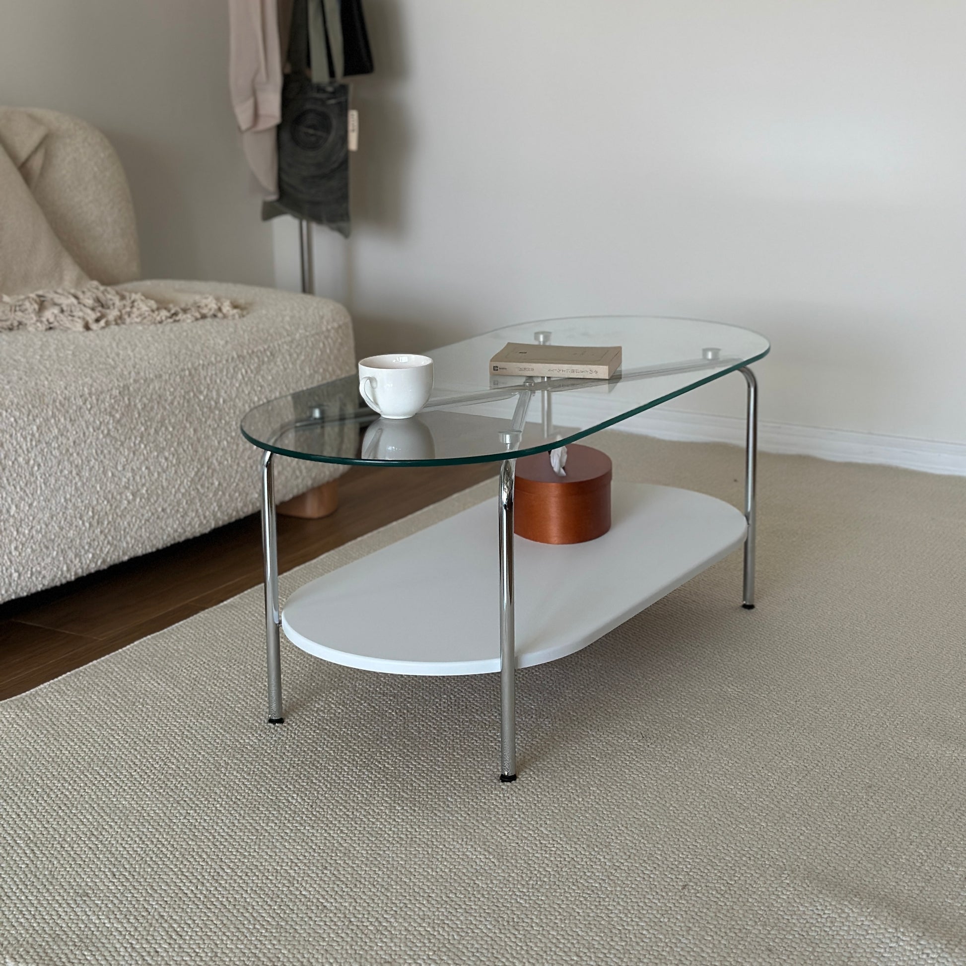 丸みのあるガラス天板のローテーブルの天板上にはコップと文庫本が置かれており、下の棚にはティッシュケースが置かれてある