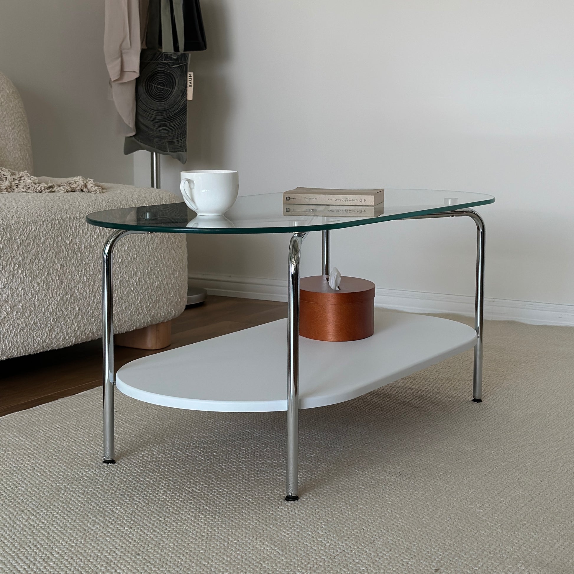 丸みのあるガラス天板のローテーブルの天板上にはコップと文庫本が置かれており、下の棚にはティッシュケースが置かれてある