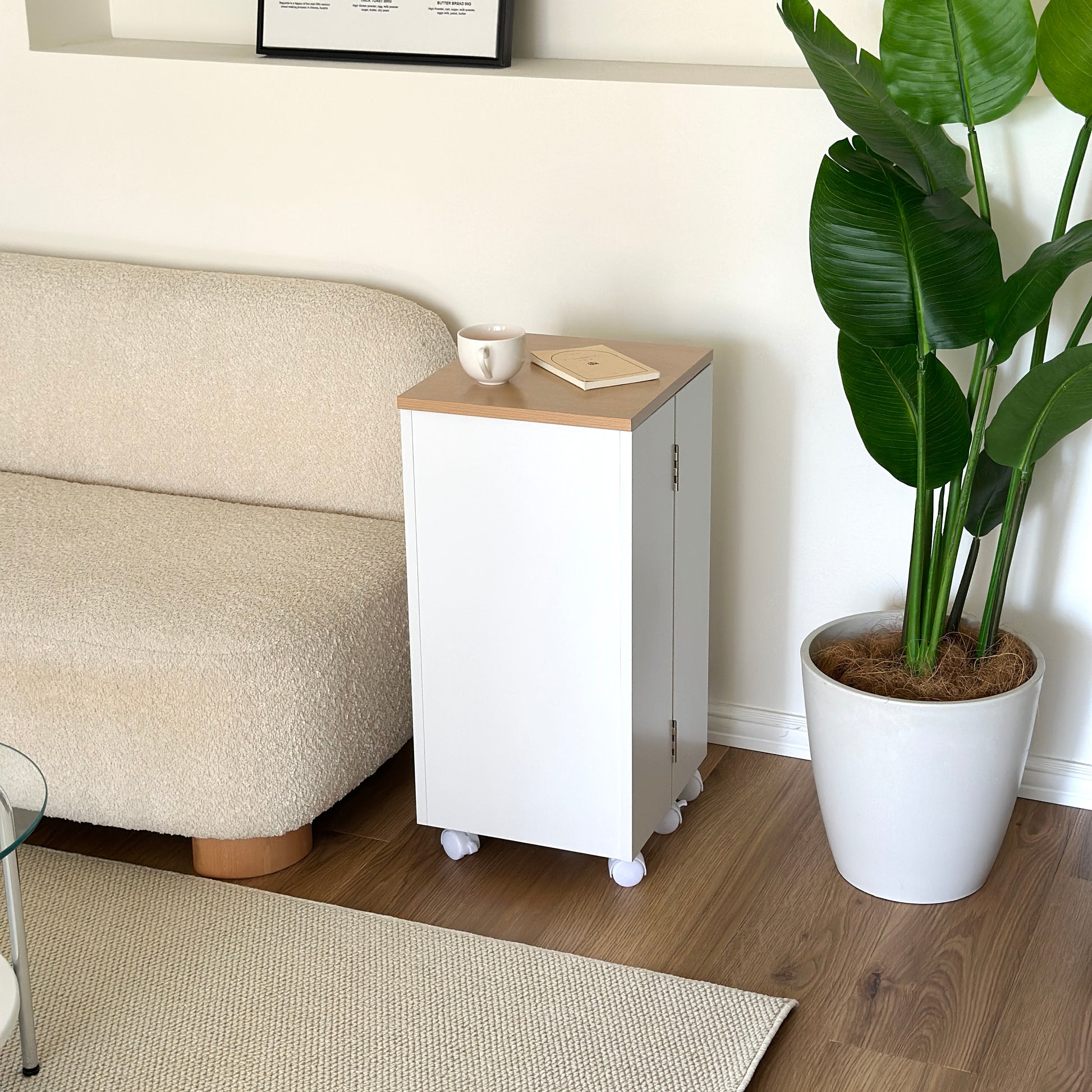 ホワイトのキャスター付きコスメワゴンの上に文庫本とコップを置いて、ソファーサイドに置いている様子