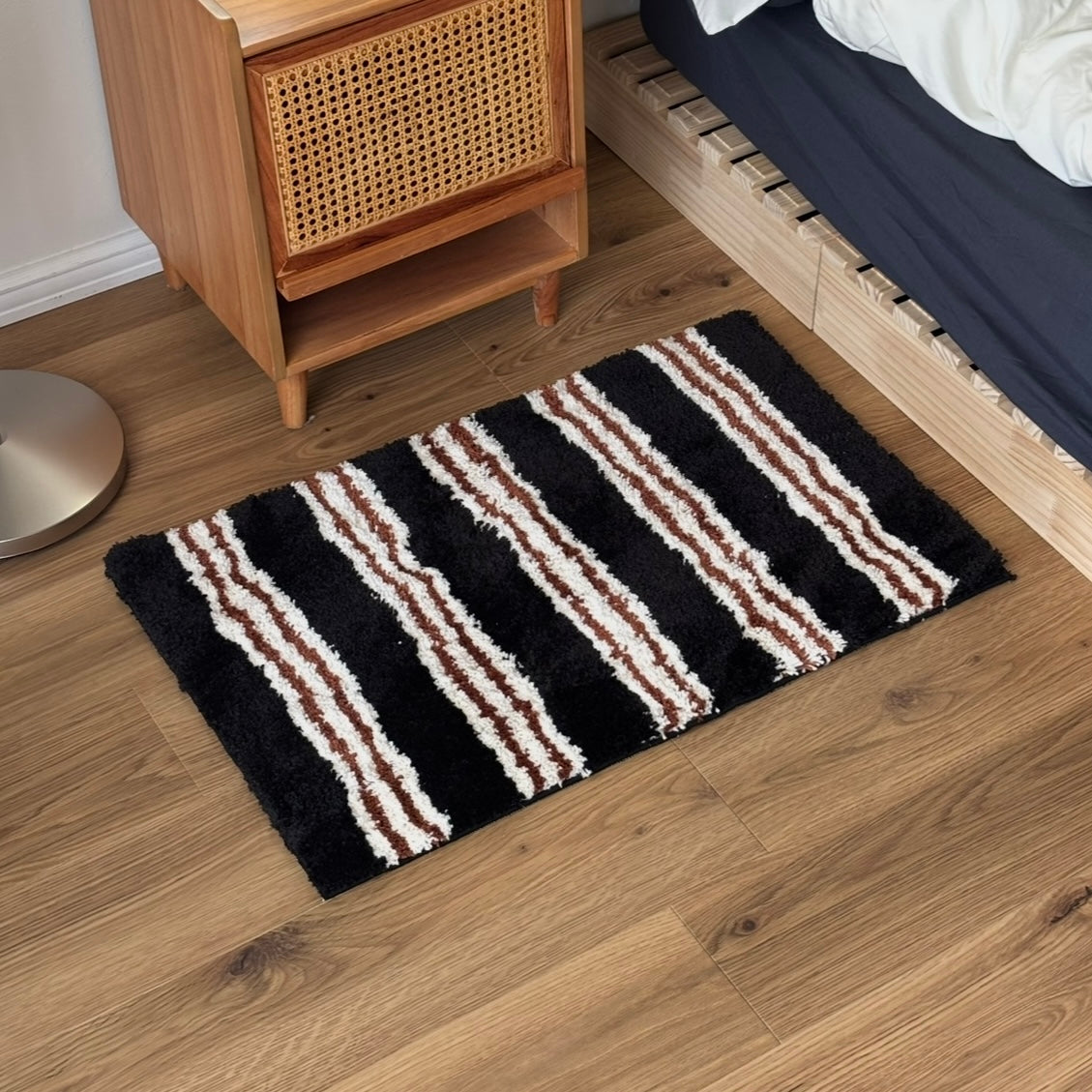 黒のストライプ柄のミニラグをラタン調のサイドテーブルの前に敷いている様子