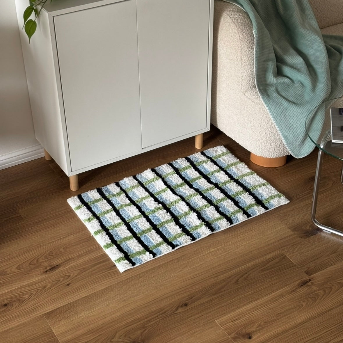 ブラックとグリーンとブルーの3色が入ったチェック柄のミニラグを白棚の前に敷いている様子