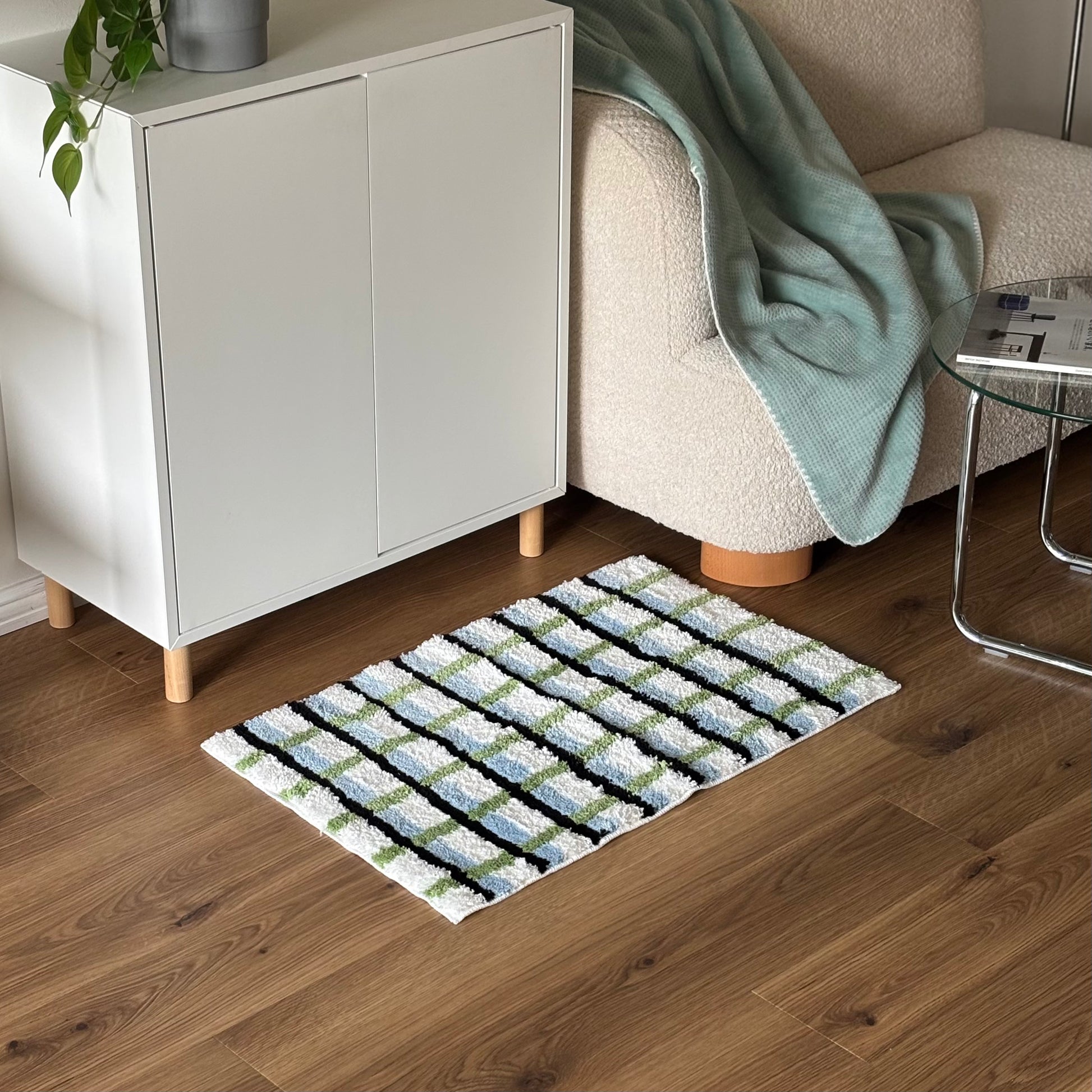 ブラックとグリーンとブルーの3色が入ったチェック柄のミニラグを白棚の前に敷いている様子