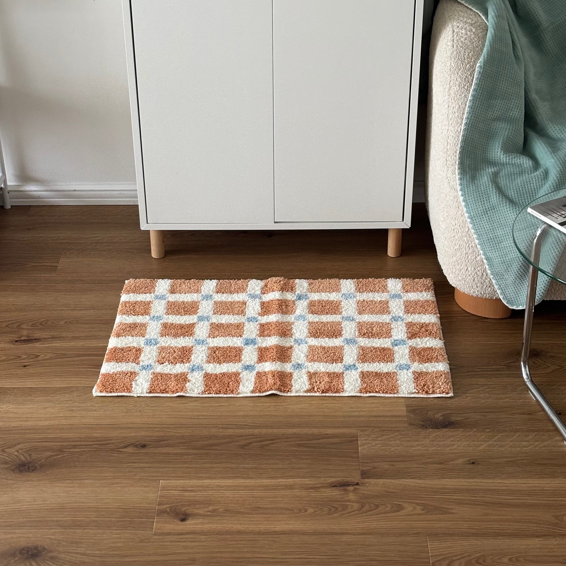 オレンジとブルーのスクエア柄のミニラグを白棚の前に敷いている様子