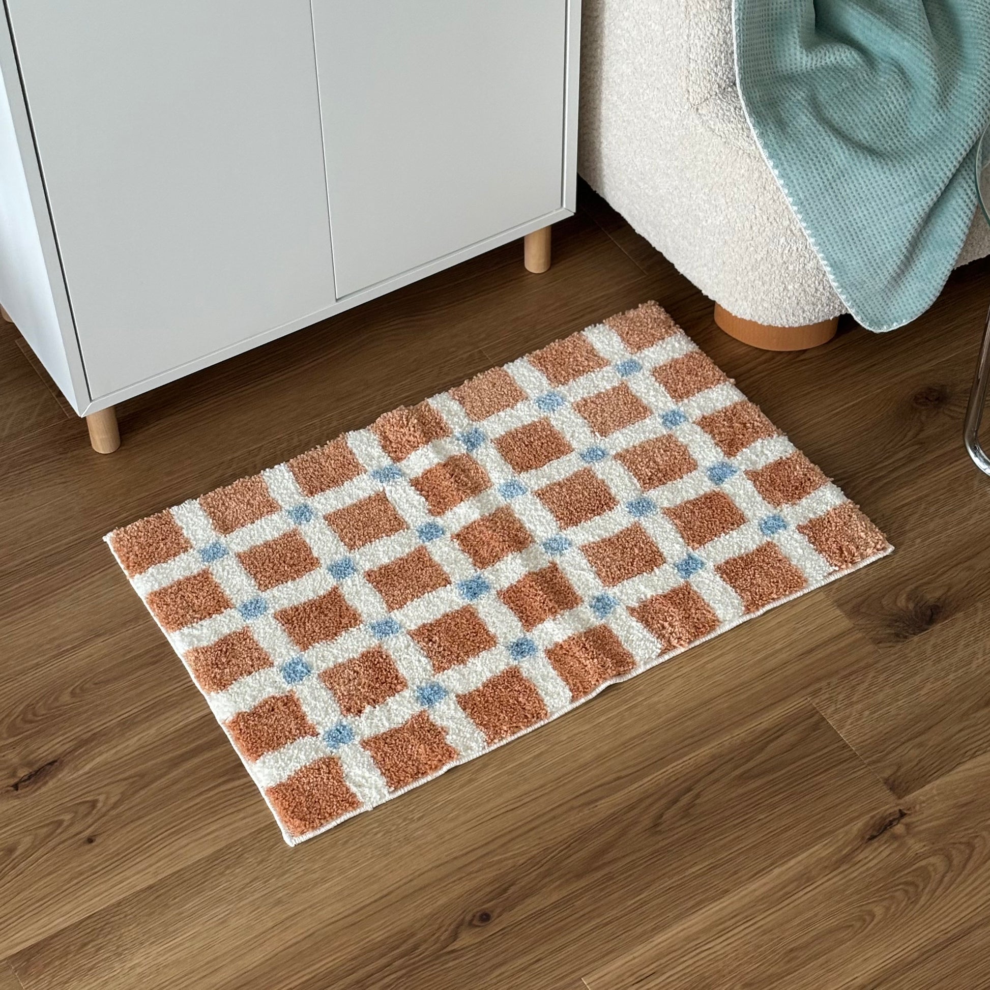 オレンジとブルーのスクエア柄のミニラグを白棚の前に敷いている様子