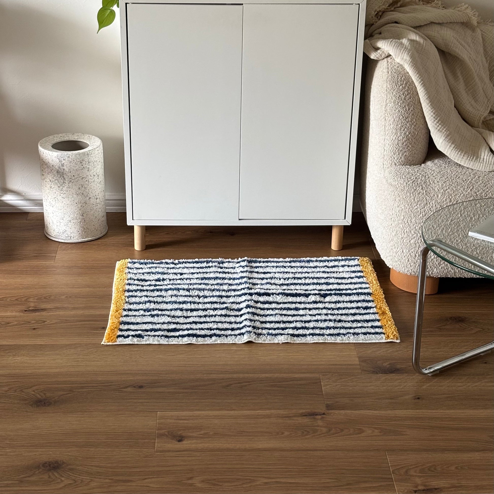 ブルーのボーダーとイエローの縁取りのミニラグを白棚の前に敷いている様子