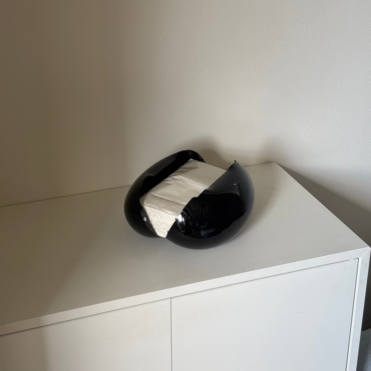 光沢のある丸みを帯びたブラックのティッシュケースを開いて、白い棚の上に置いている様子