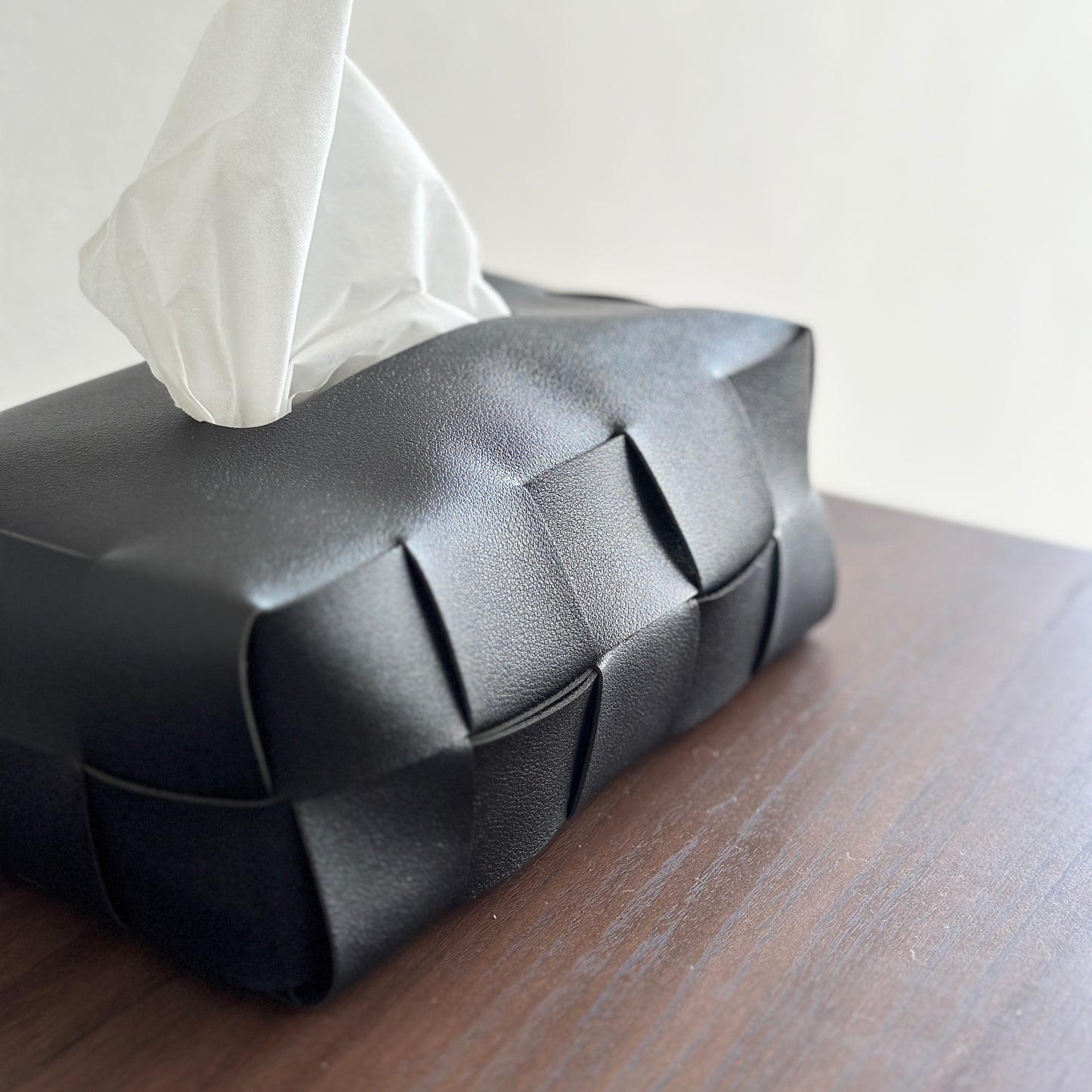 黒いレザーの編み込みのティッシュボックスが茶色の棚の上に置かれている様子