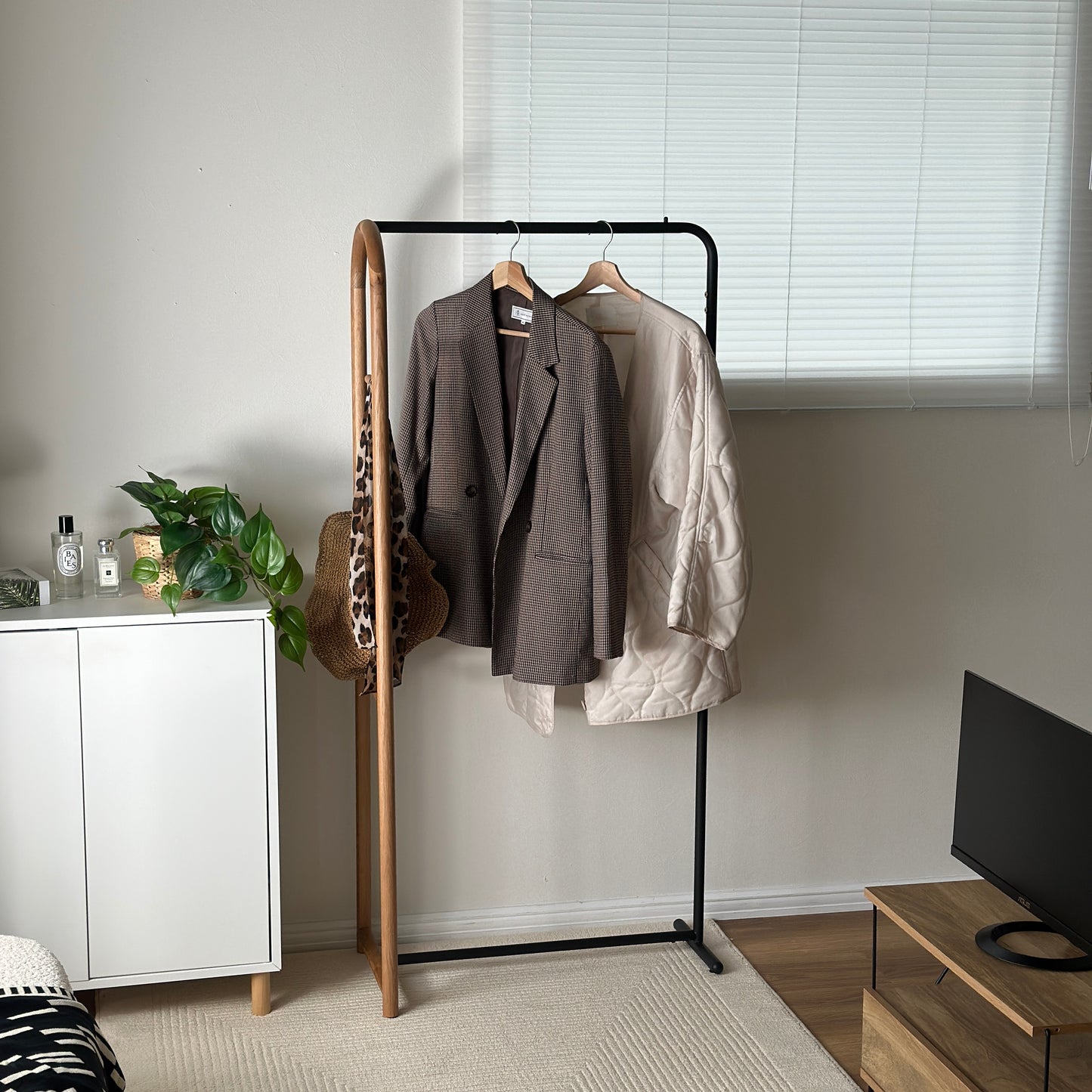 オーク材とブラックスチールのハンガーラックにスカーフや帽子、アウターがかかっている様子