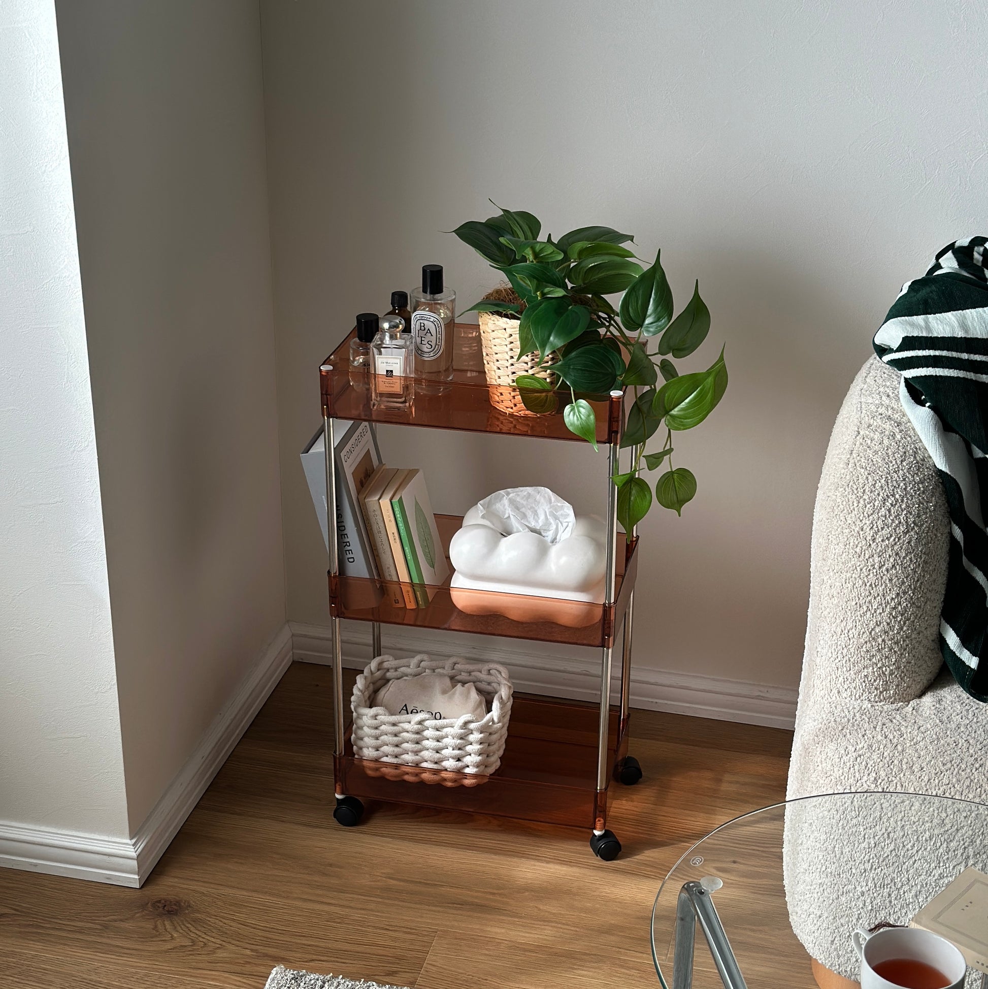 クリアなブラウンの3段シェルフに香水や植物、ティッシュケース、本などが置かれてある様子