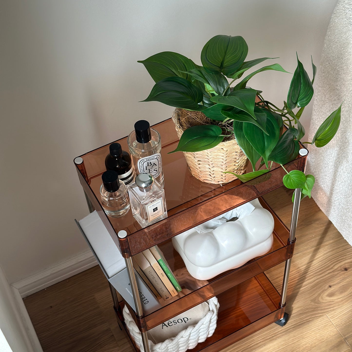 クリアなブラウンの3段シェルフに香水や植物、ティッシュケース、本などが置かれてある様子