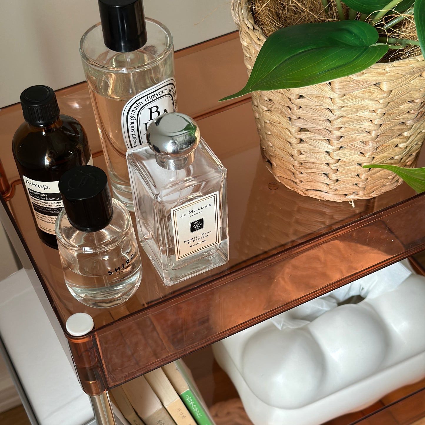 クリアなブラウンの3段シェルフに植物や香水、本、ティッシュケースなどが置かれてある様子