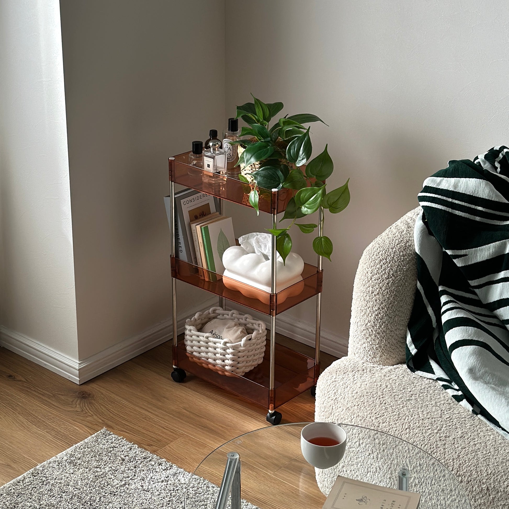 クリアなブラウンの3段シェルフに香水や植物、ティッシュケース、本などが置かれてある様子