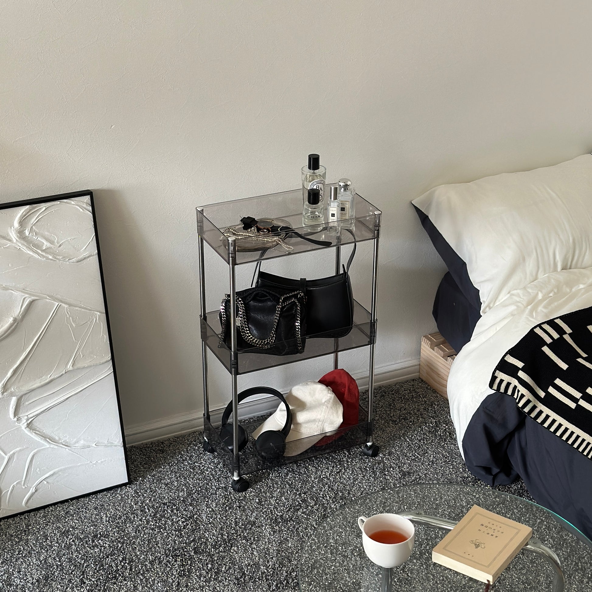 クリアなブラックの3段シェルフにバッグや帽子、ヘッドフォン、香水、アクセサリーが置いてある様子