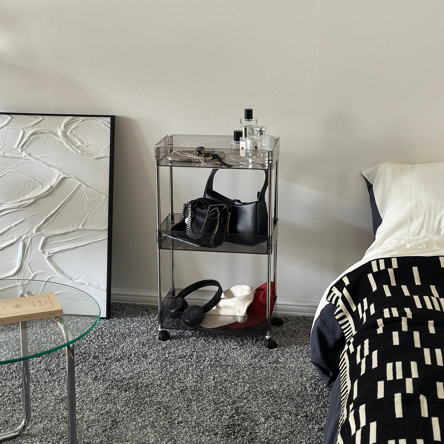 クリアなブラックの3段シェルフにバッグや帽子、ヘッドフォン、香水、アクセサリーが置かれてある様子