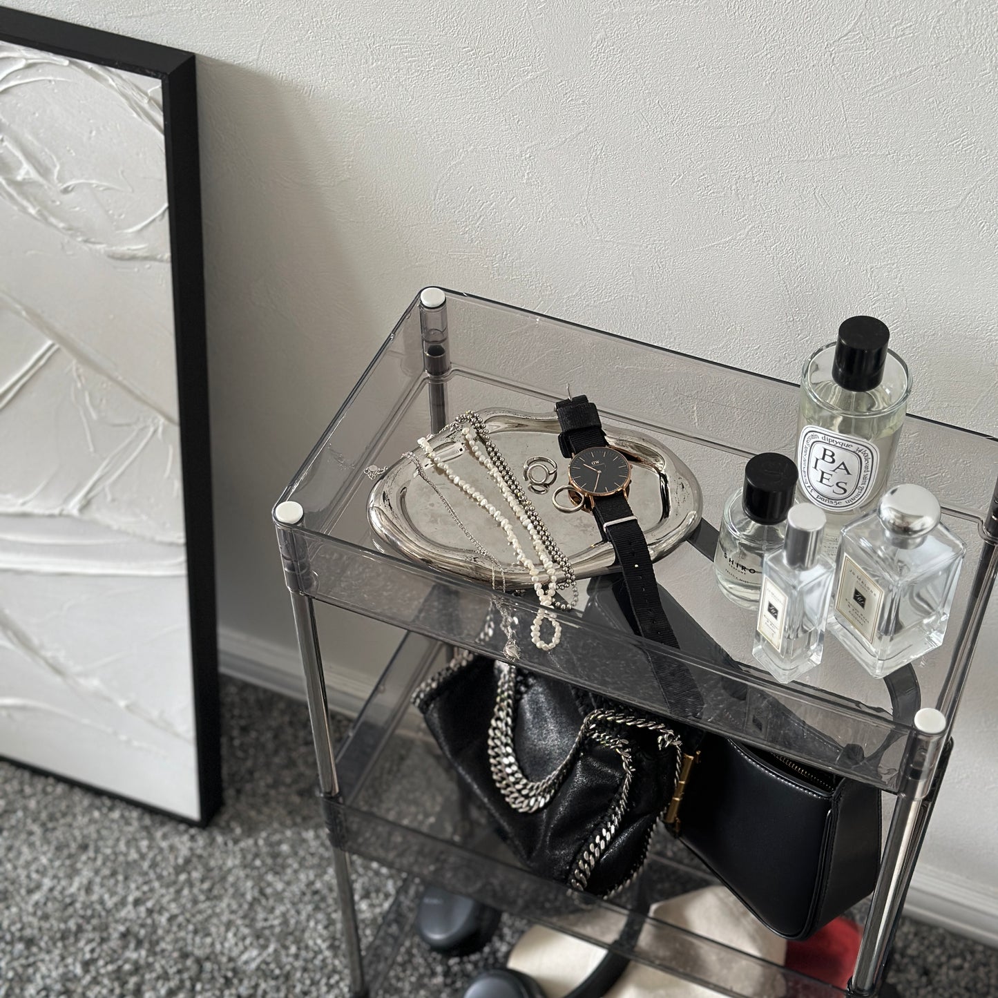 クリアなブラックの3段シェルフにバッグや帽子、ヘッドフォン、香水、アクセサリーが置かれてある様子