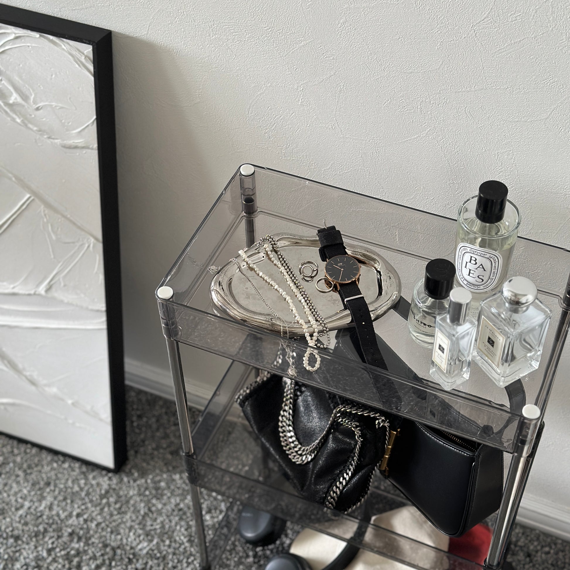 クリアなブラックの3段シェルフにバッグや帽子、ヘッドフォン、香水、アクセサリーが置かれてある様子