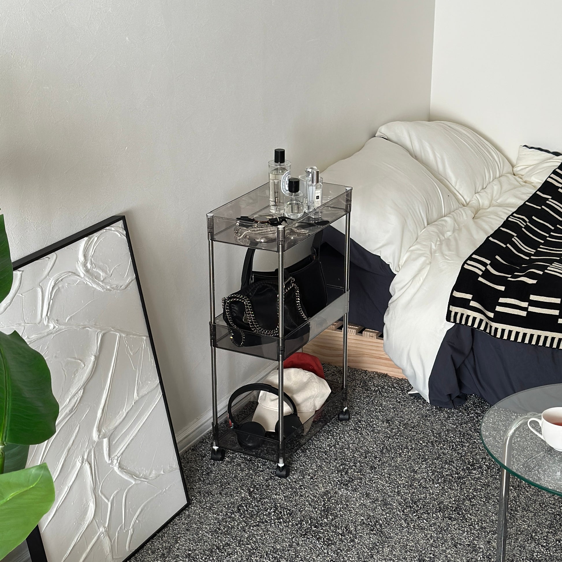 クリアなブラックの3段シェルフにバッグや帽子、ヘッドフォン、香水、アクセサリーが置かれてある様子