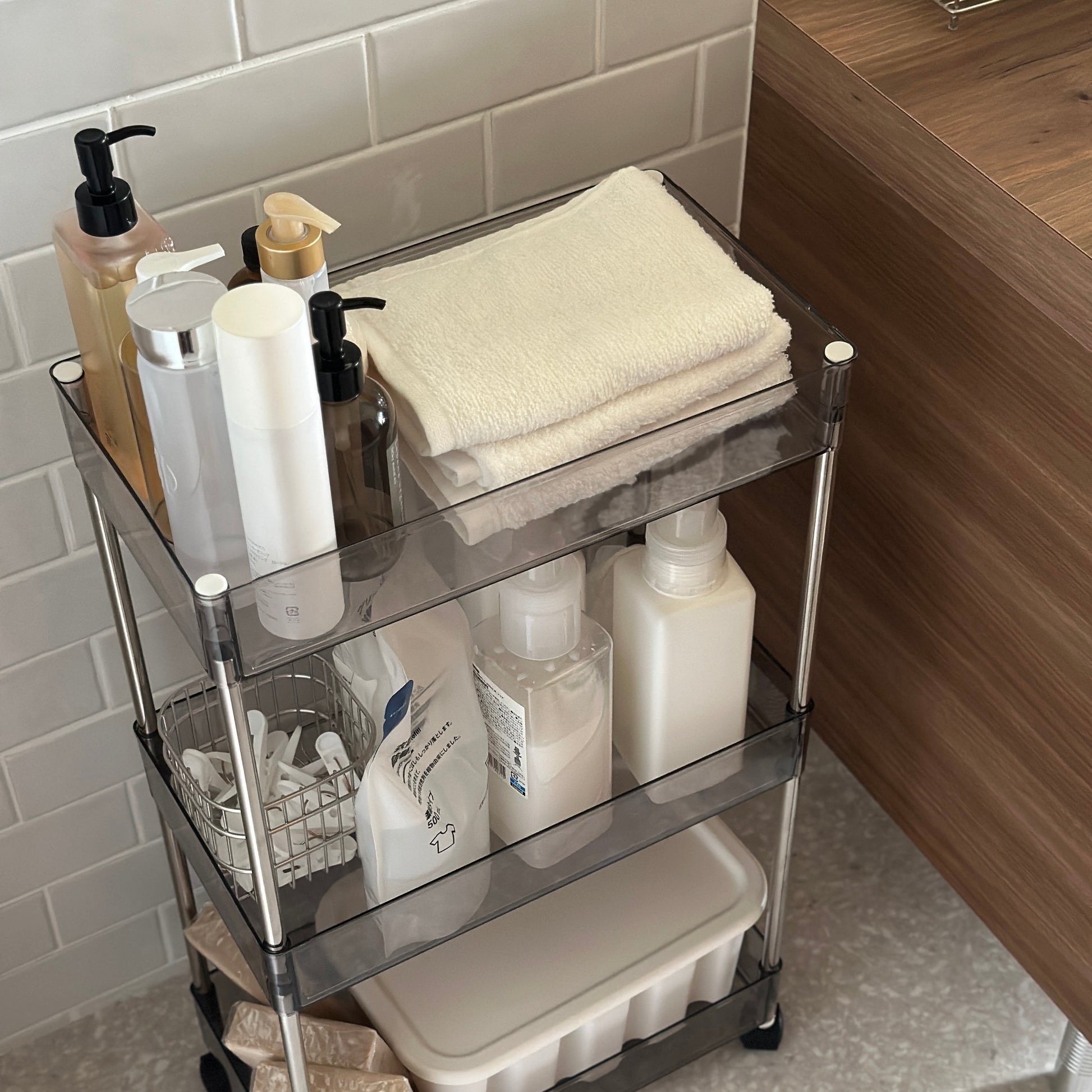 クリアなブラックの3段シェルフにスキンケア用品やタオル、洗濯洗剤などが収納され、洗面所に置かれてある様子