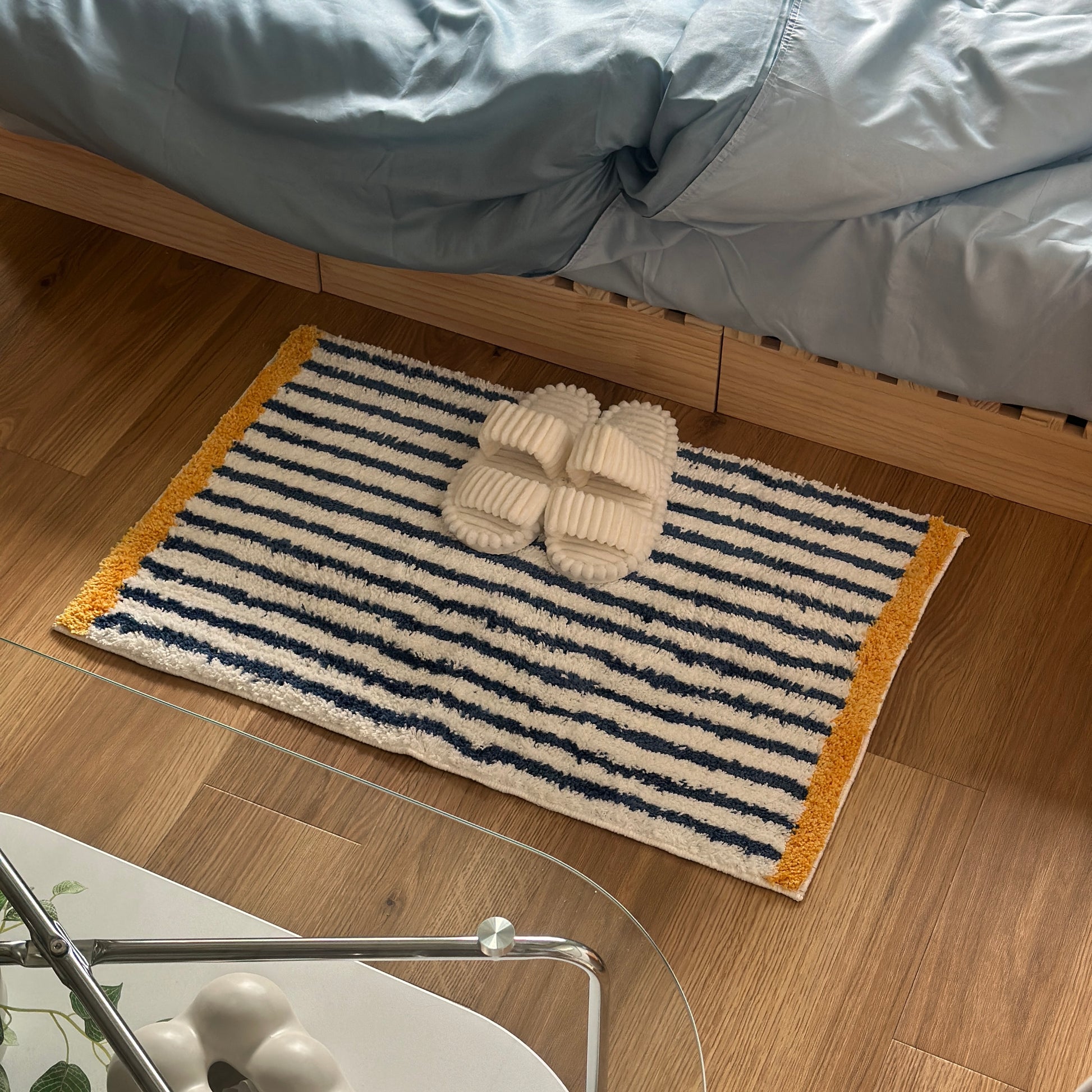 ブルーのボーダーとイエローの縁取りのミニラグをベッド横に敷いている様子