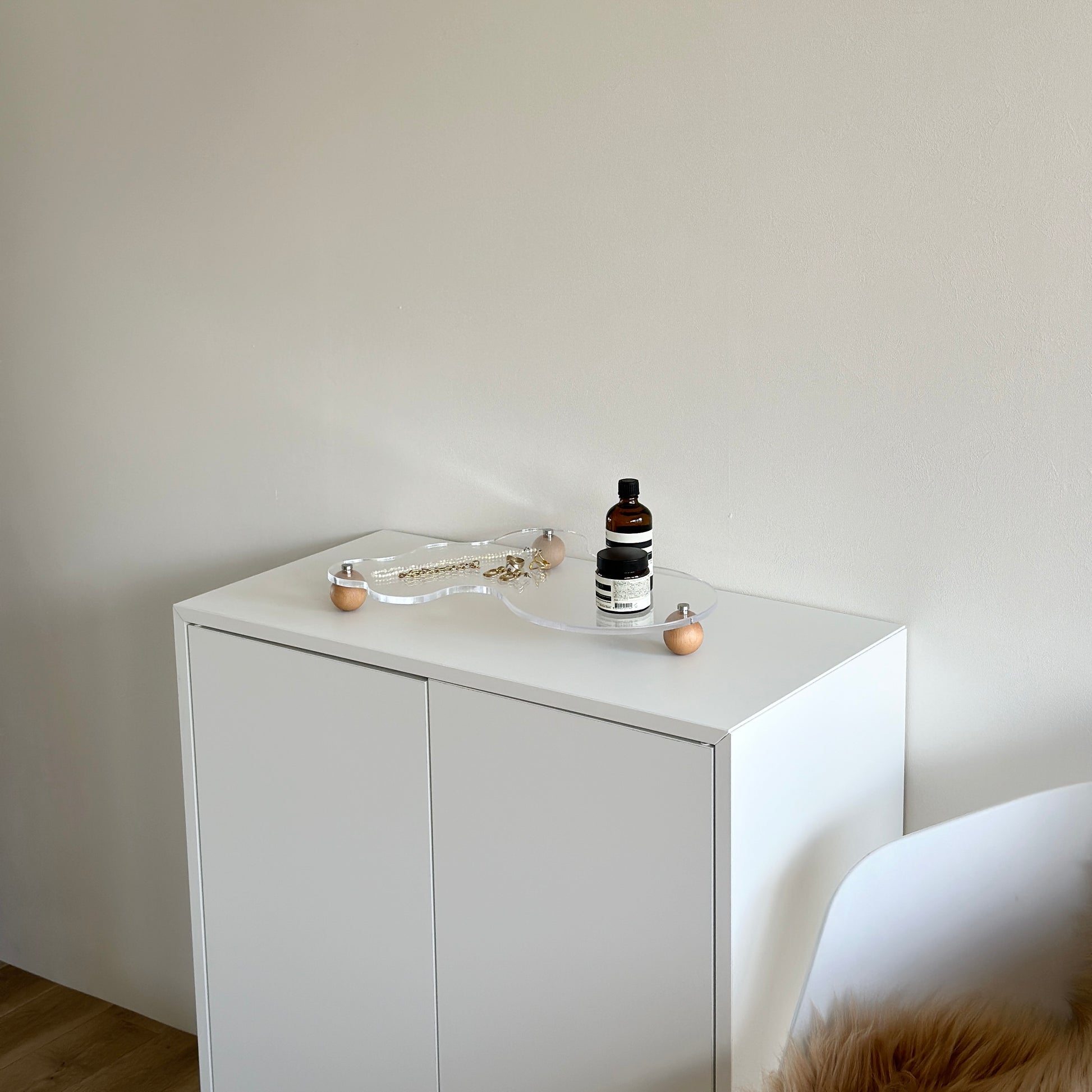 ウッドボールの脚がついたアクリルトレイの上にアクセサリーやフレグランスを置いている様子