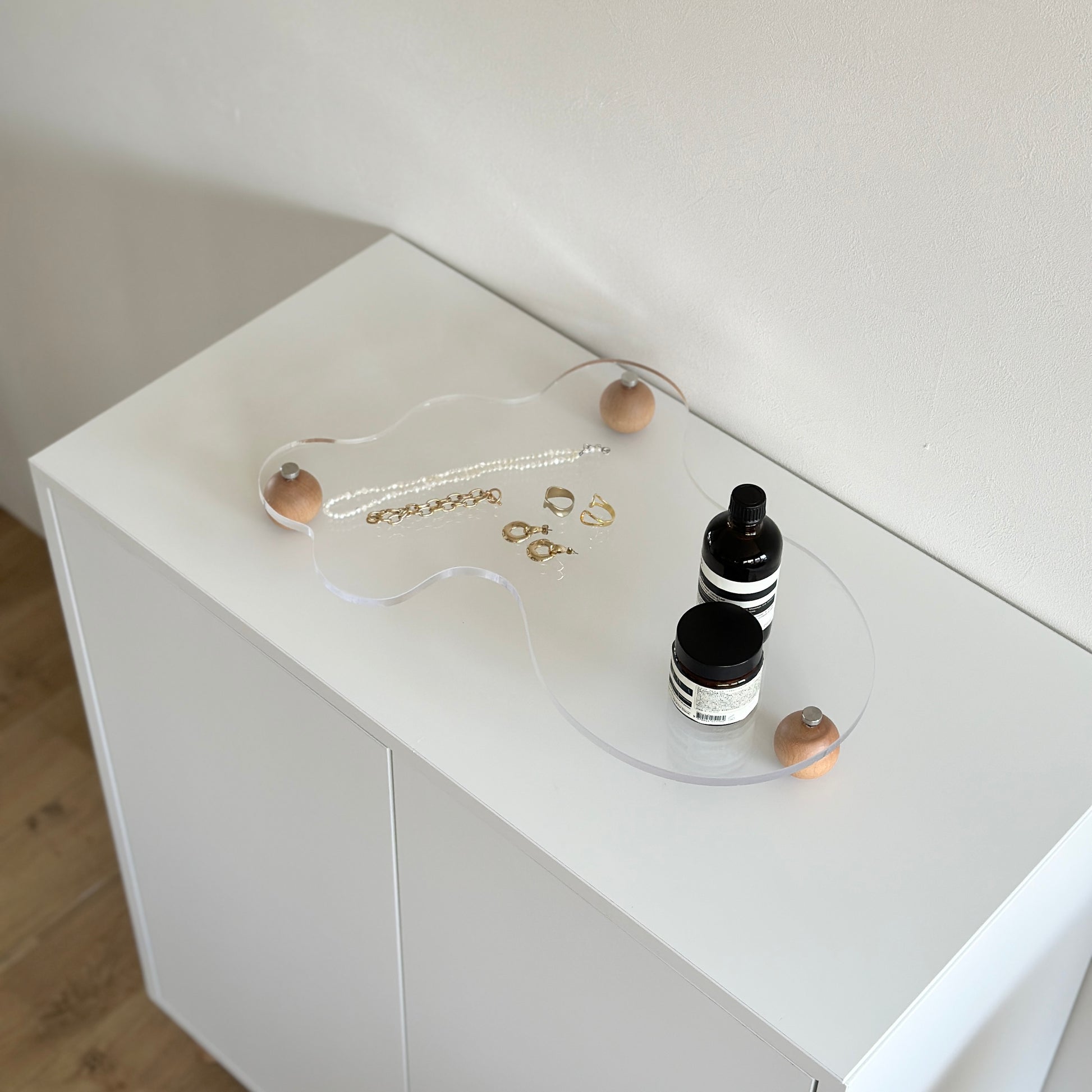 ウッドボールの脚がついたアクリルトレイの上にフレグランスやアクセサリーを置いている様子