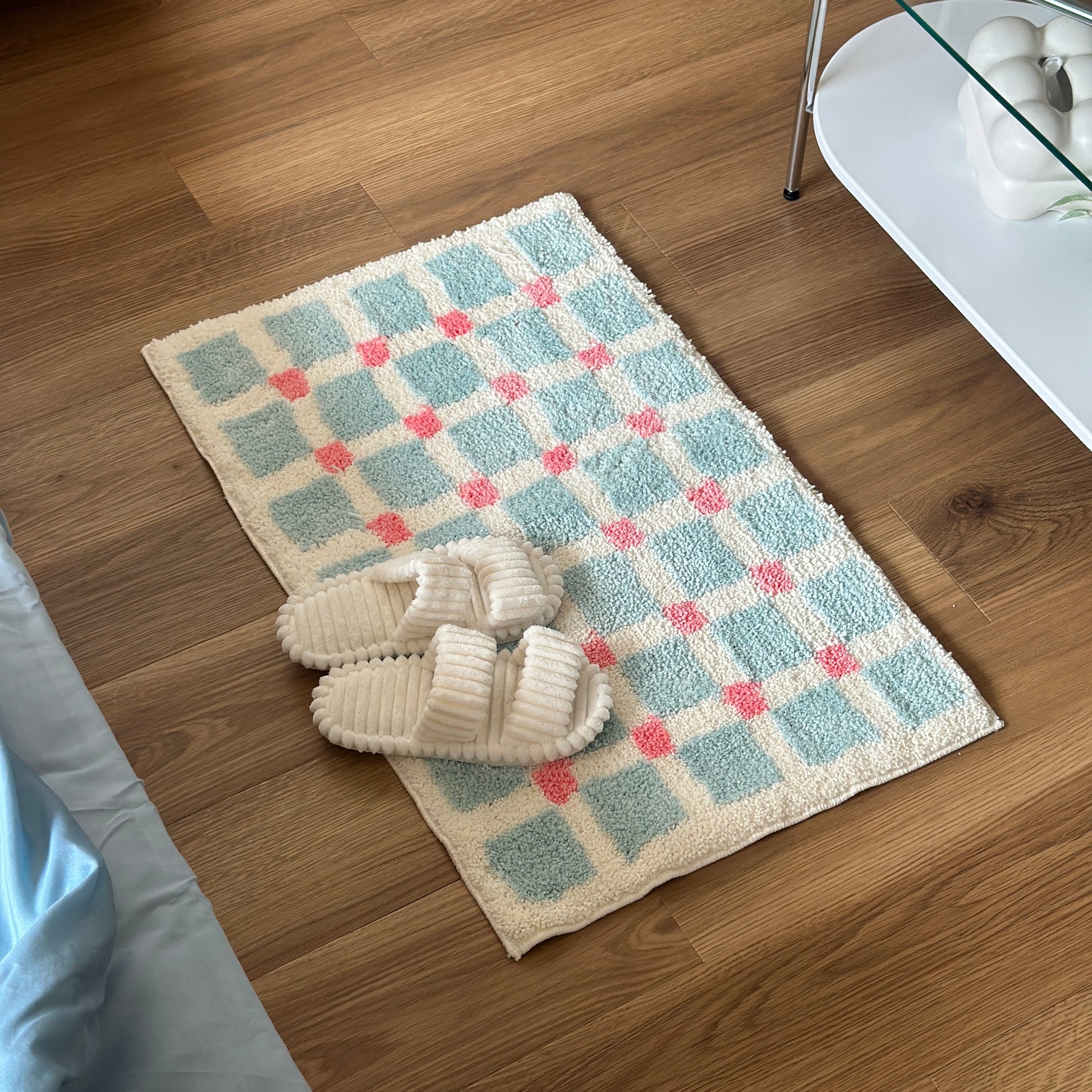 ライトブルーとピンクのスクエア柄のミニラグの上にホワイトのスリッパが置かれている様子