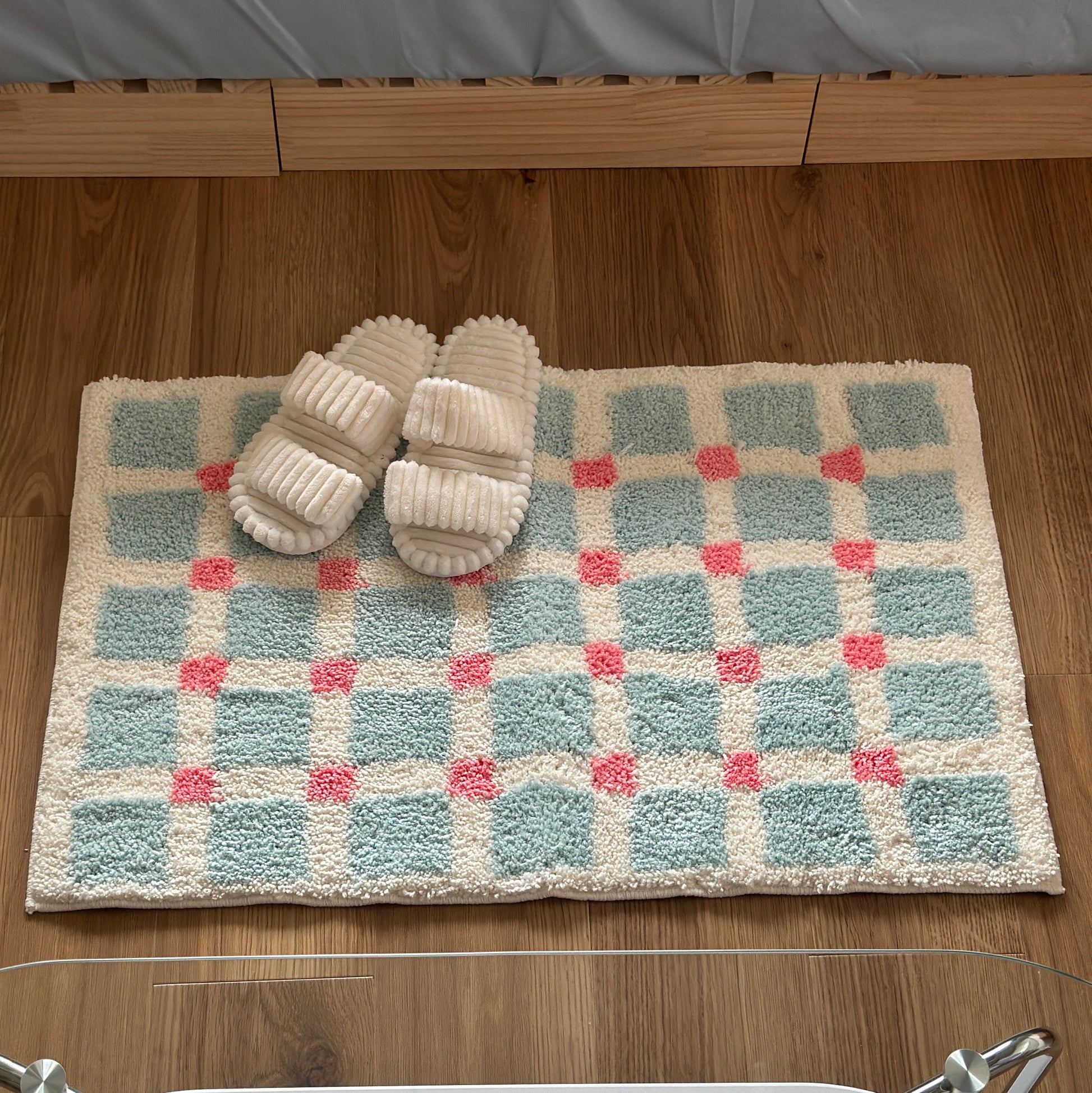 ライトブルーとピンクのスクエア柄のミニラグの上にホワイトのスリッパが置かれている様子