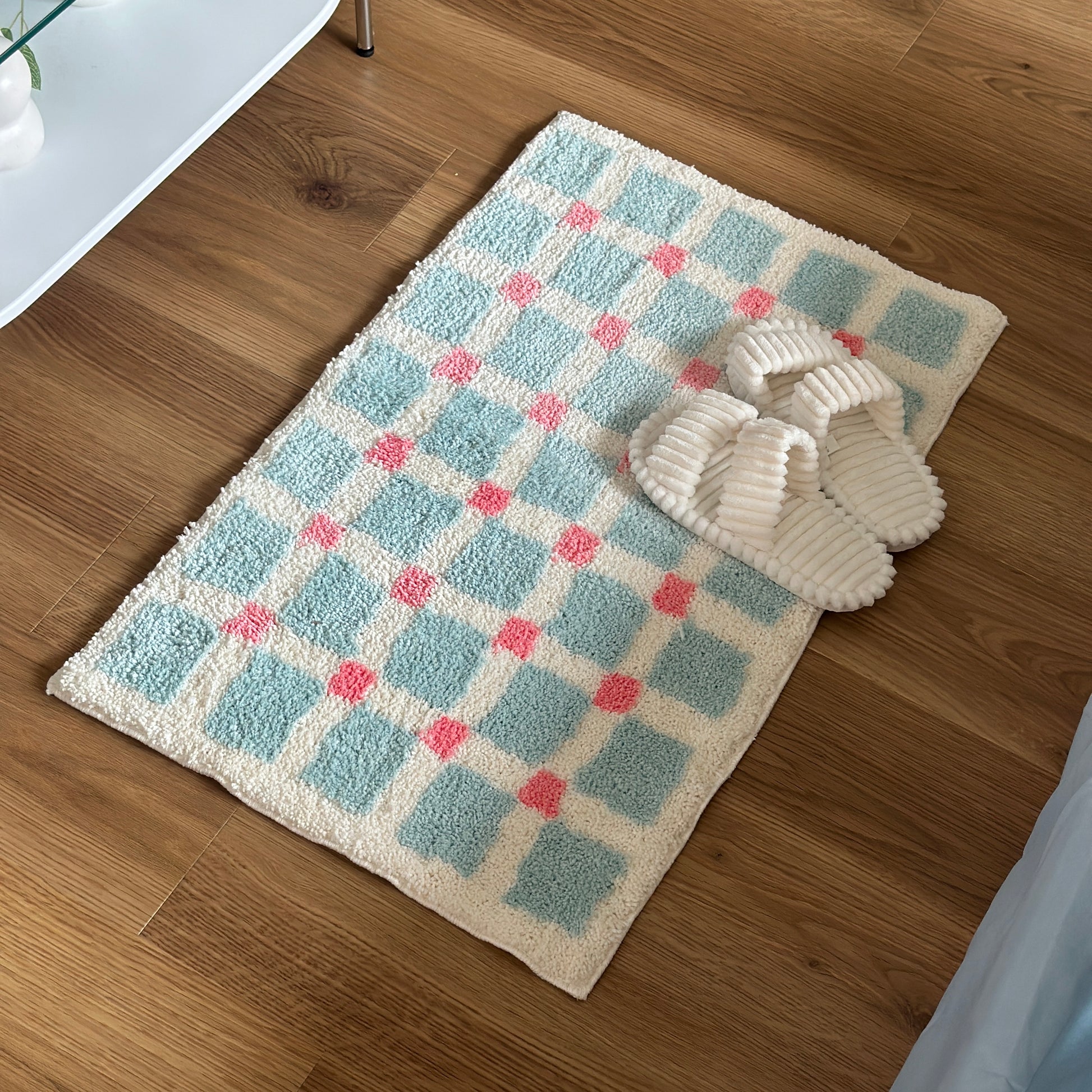 ライトブルーとピンクのスクエア柄のミニラグの上にホワイトのスリッパが置かれている様子