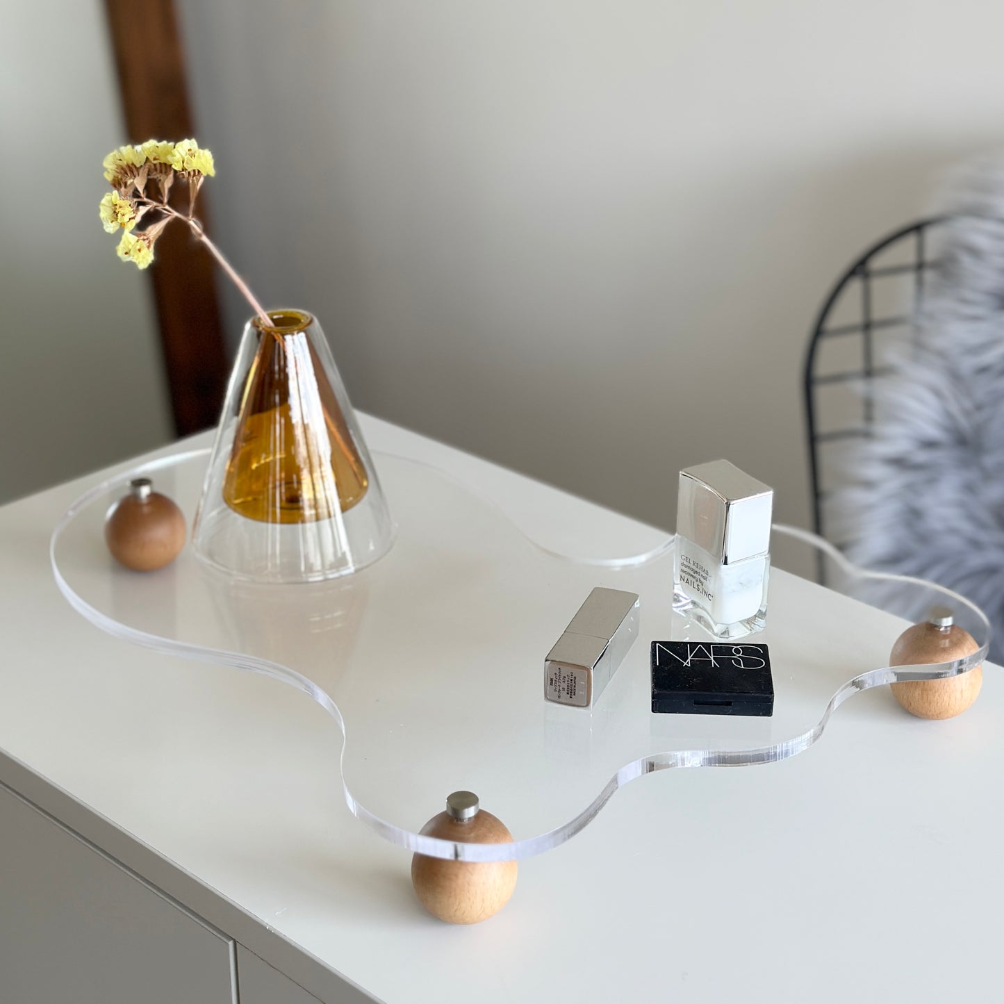 ウッドボールの脚がついたアクリルトレイの上にフラワーベースや化粧品を置いている様子