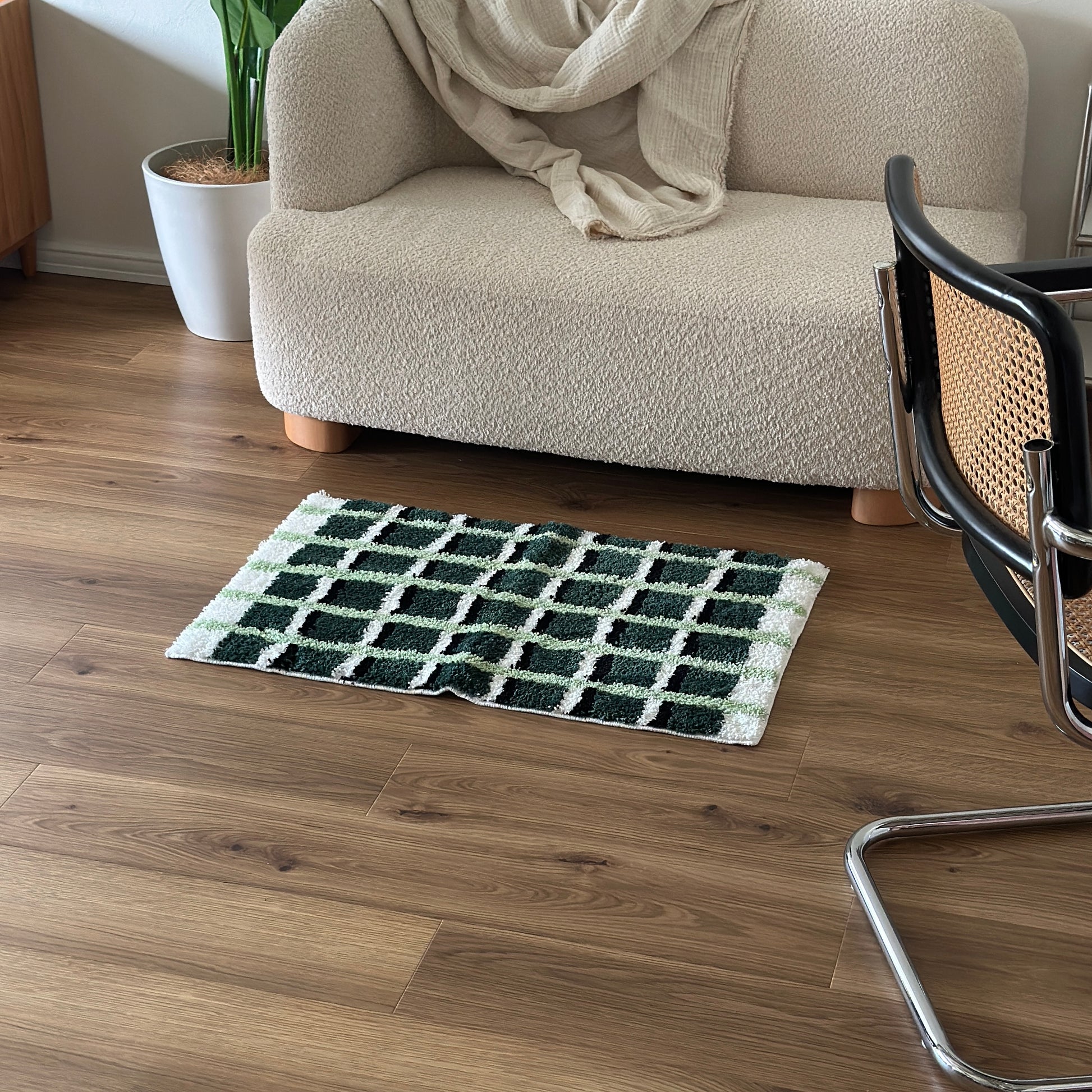 黄緑と深緑とブラックの3色が入ったチェック柄のミニラグをソファ前に敷いている様子