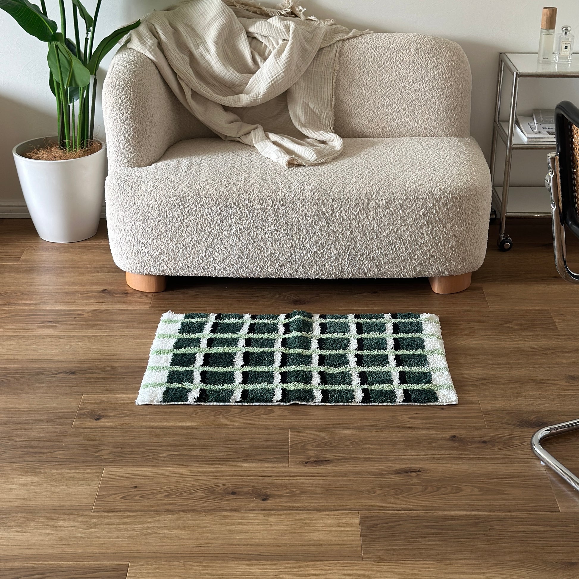 黄緑と深緑とブラックの3色が入ったチェック柄のミニラグをソファ前に敷いている様子