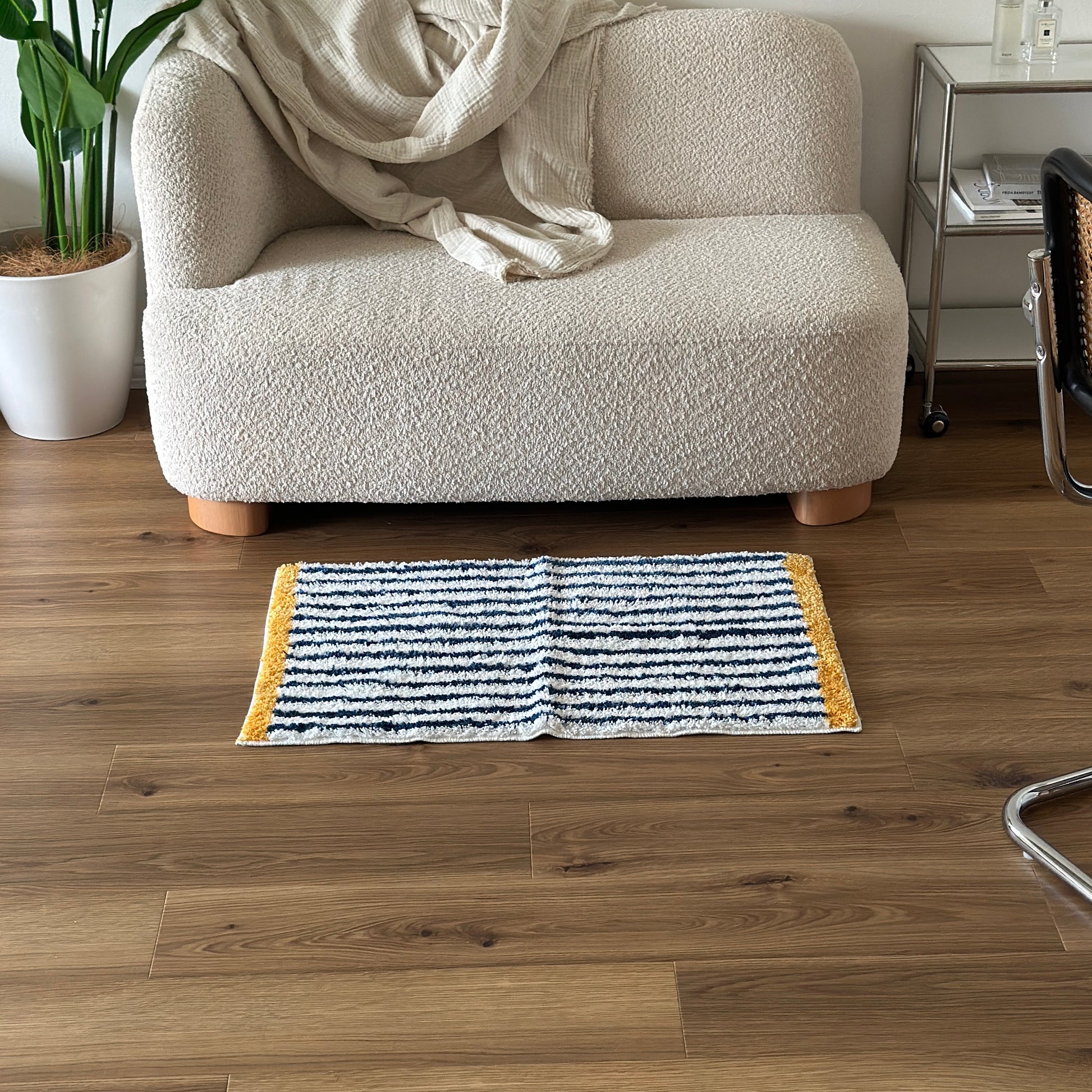 ブルーのボーダーとイエローの縁取りのミニラグをソファ前に敷いている様子