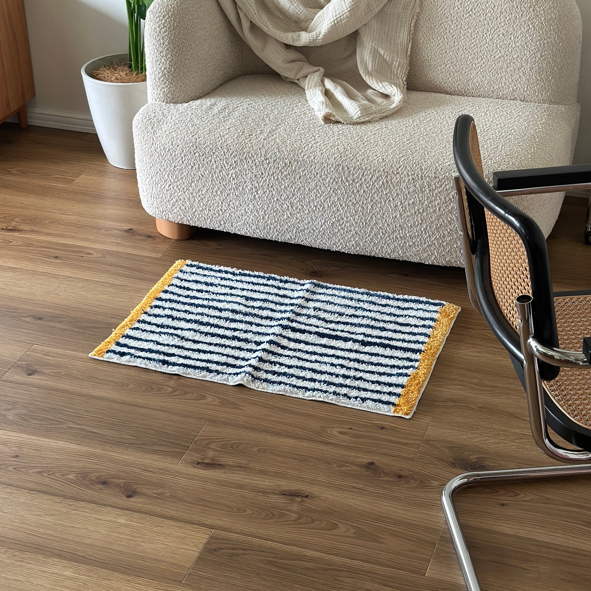 ブルーのボーダーとイエローの縁取りのミニラグをソファ前に置いている様子