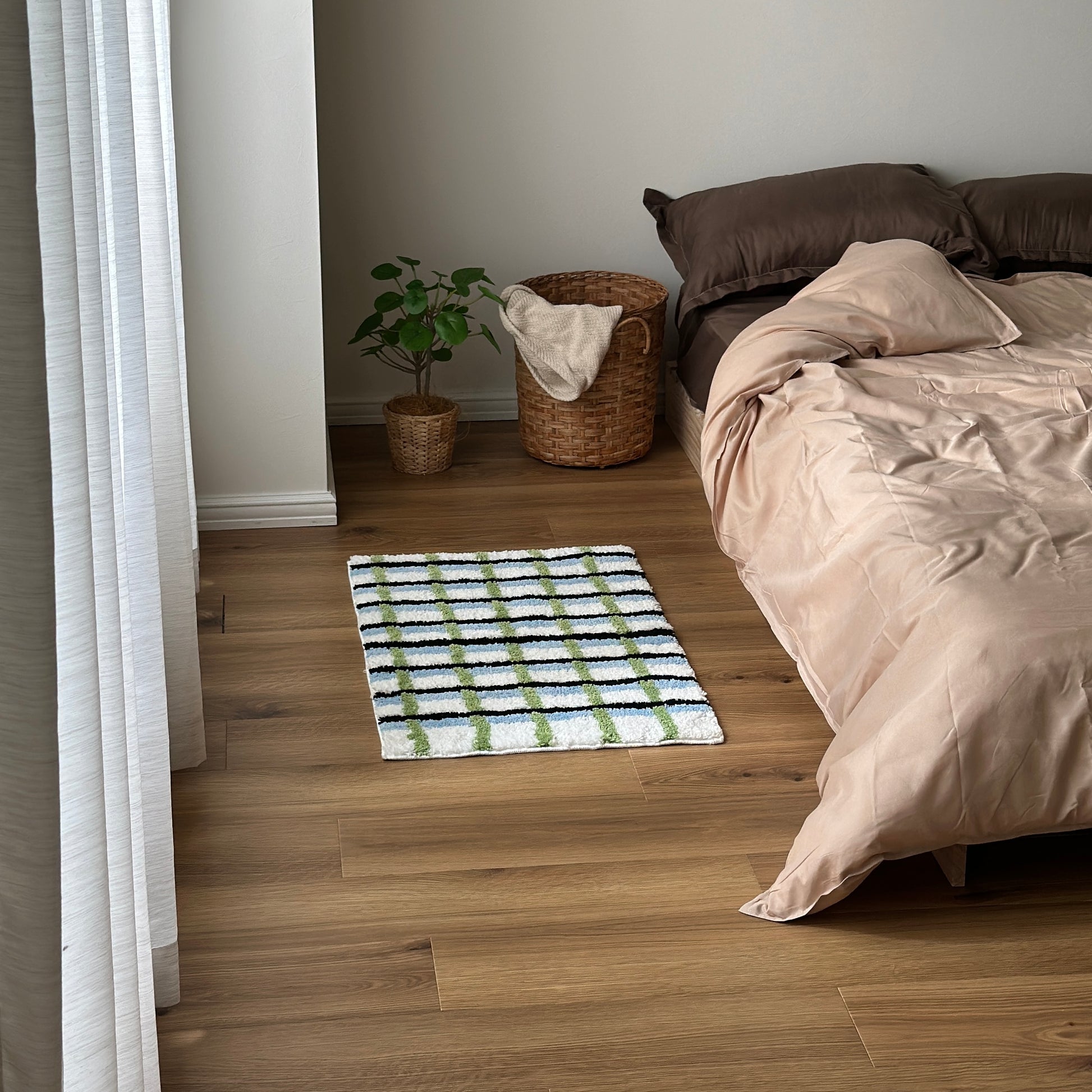 ブラックとグリーンとブルーの3色が入ったチェック柄のミニラグをベッド横に敷いている様子