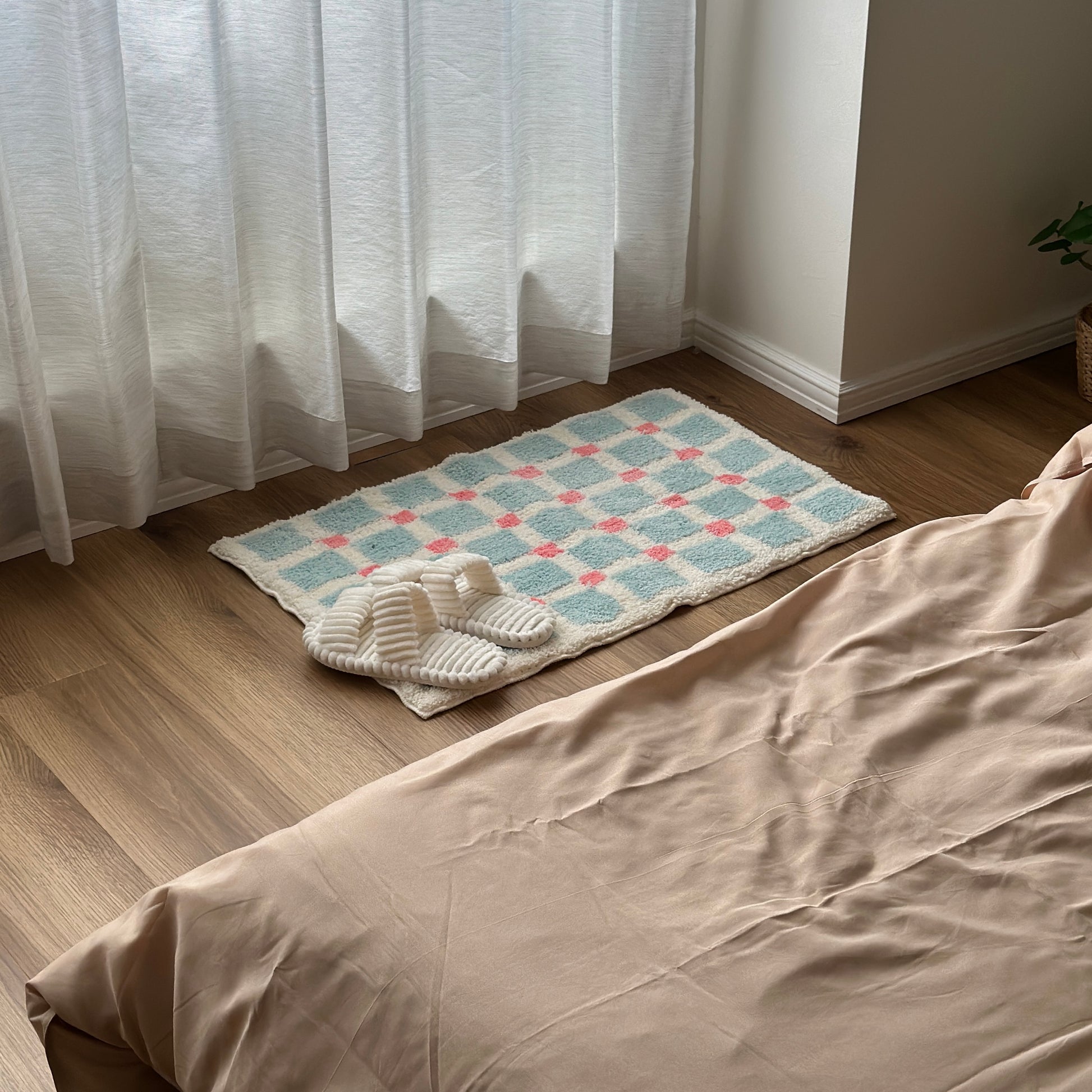 ライトブルーとピンクのスクエア柄のミニラグにホワイトのスリッパが置かれている様子