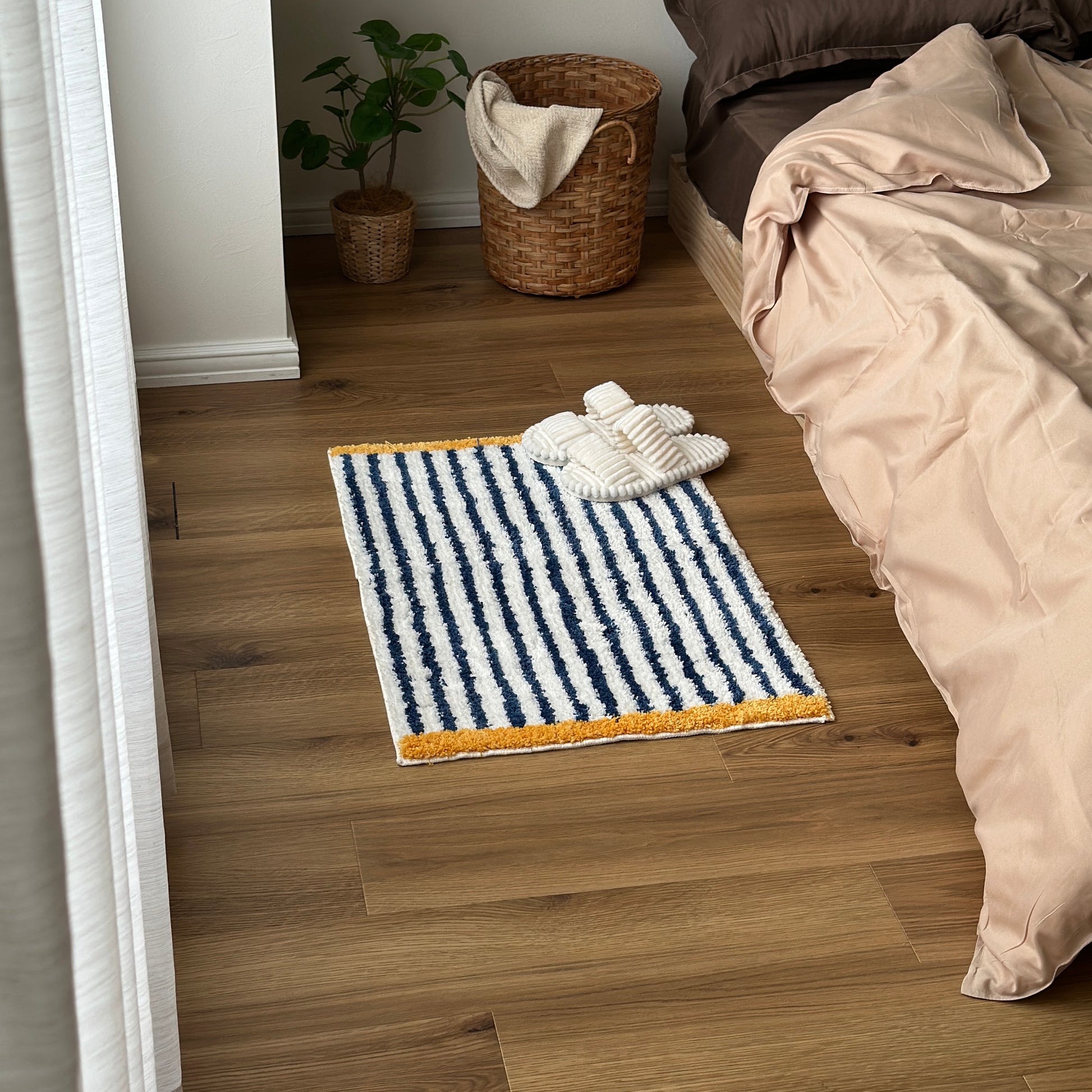 ブルーのボーダーとイエローの縁取りのミニラグをベッド横に敷いている様子