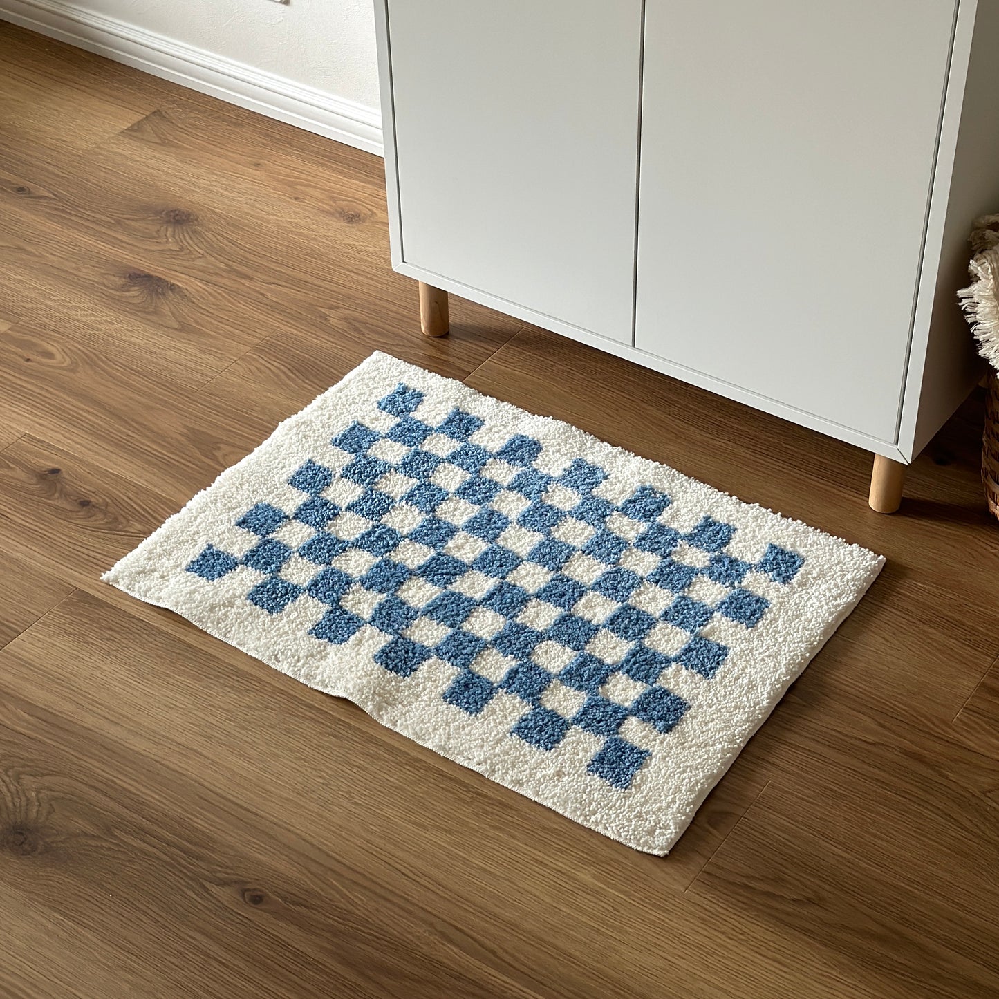 白い棚の前に青と白のチェック柄のミニラグを敷いている様子