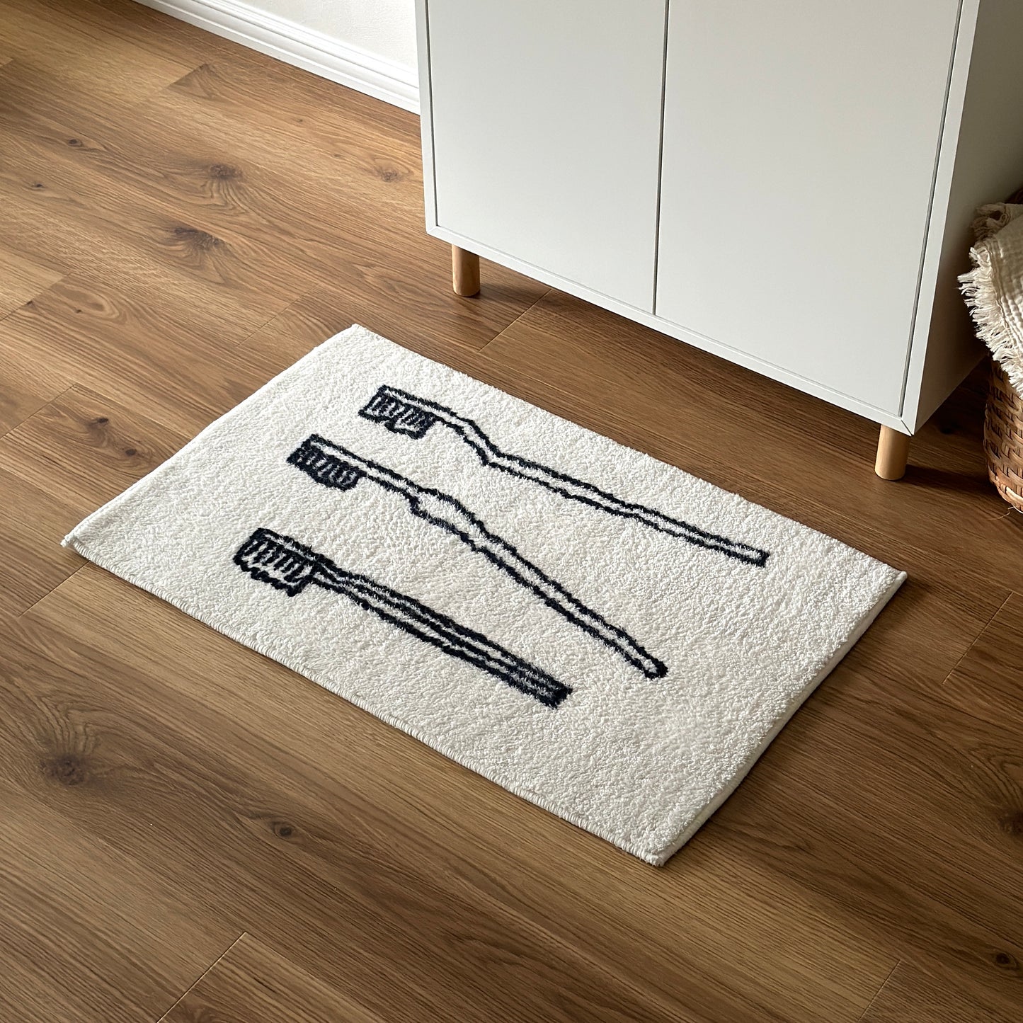 白い棚の前に歯ブラシ柄の白いラグマットが敷かれてある