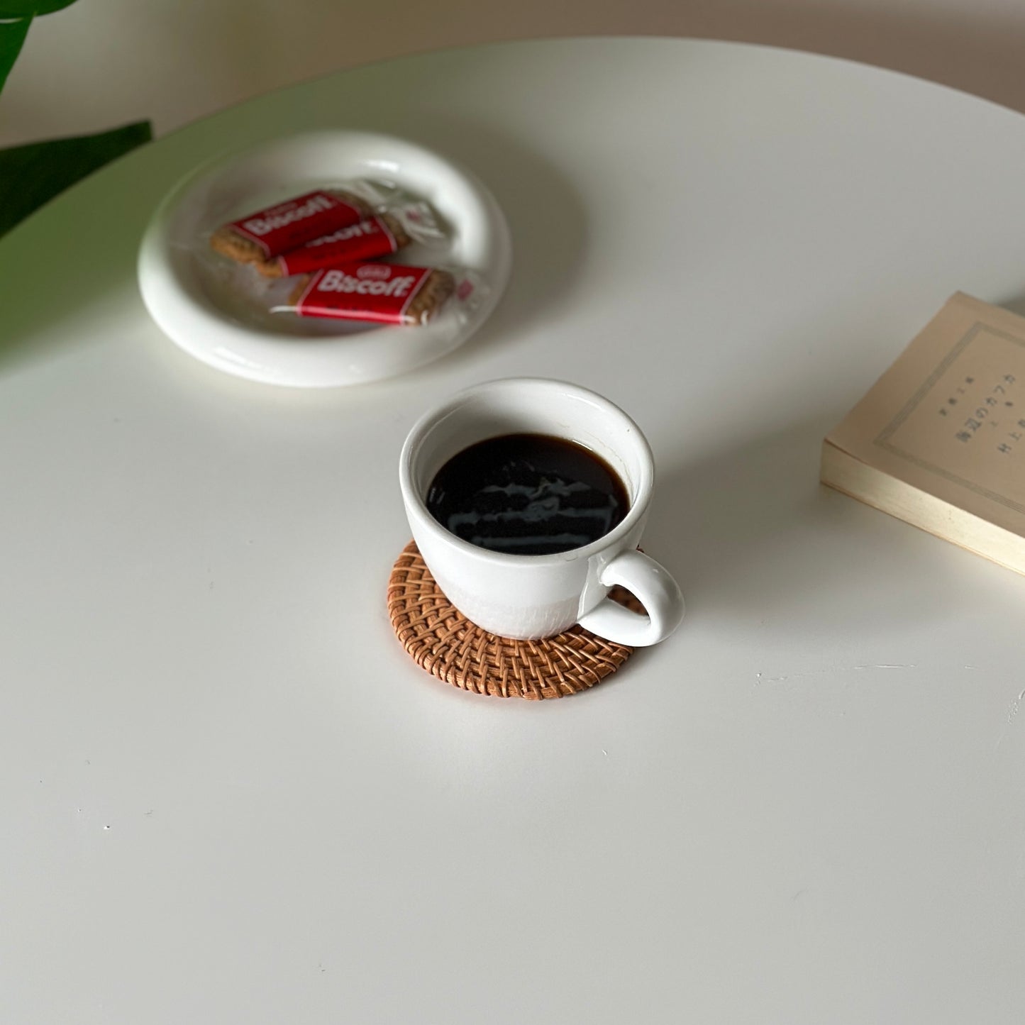 ラタンのコースターの上にコーヒーが入った白いコップが置かれてある