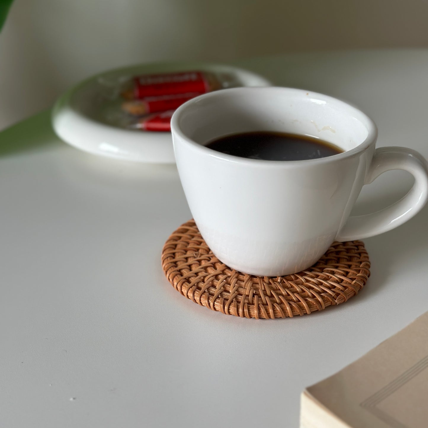 ラタンのコースターの上にコーヒーが入った白いマグカップが置かれてある