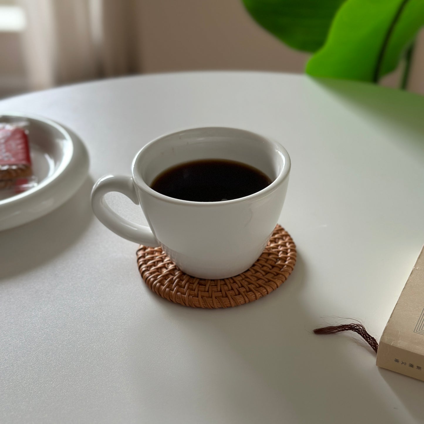 ラタンのコースターの上にコーヒーが入った白いマグカップが置かれてある