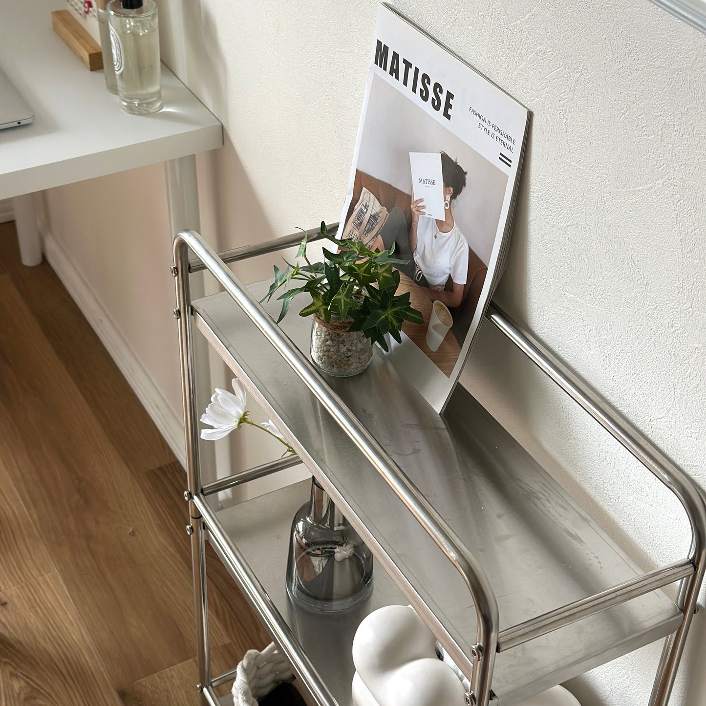 ステンレス製の3段ワゴンに雑誌や植物、花が生けられている花瓶、ティッシュなどが置かれてある
