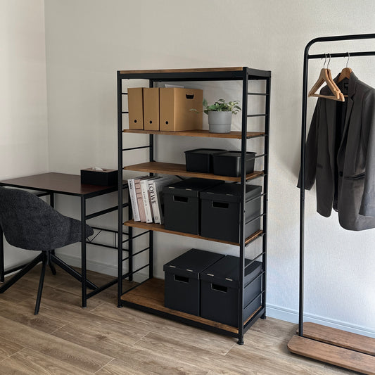 部屋の中に4段のウォルナットブラックのシェルフが置いてあり、茶色の箱や黒の箱や本が置かれている様子。