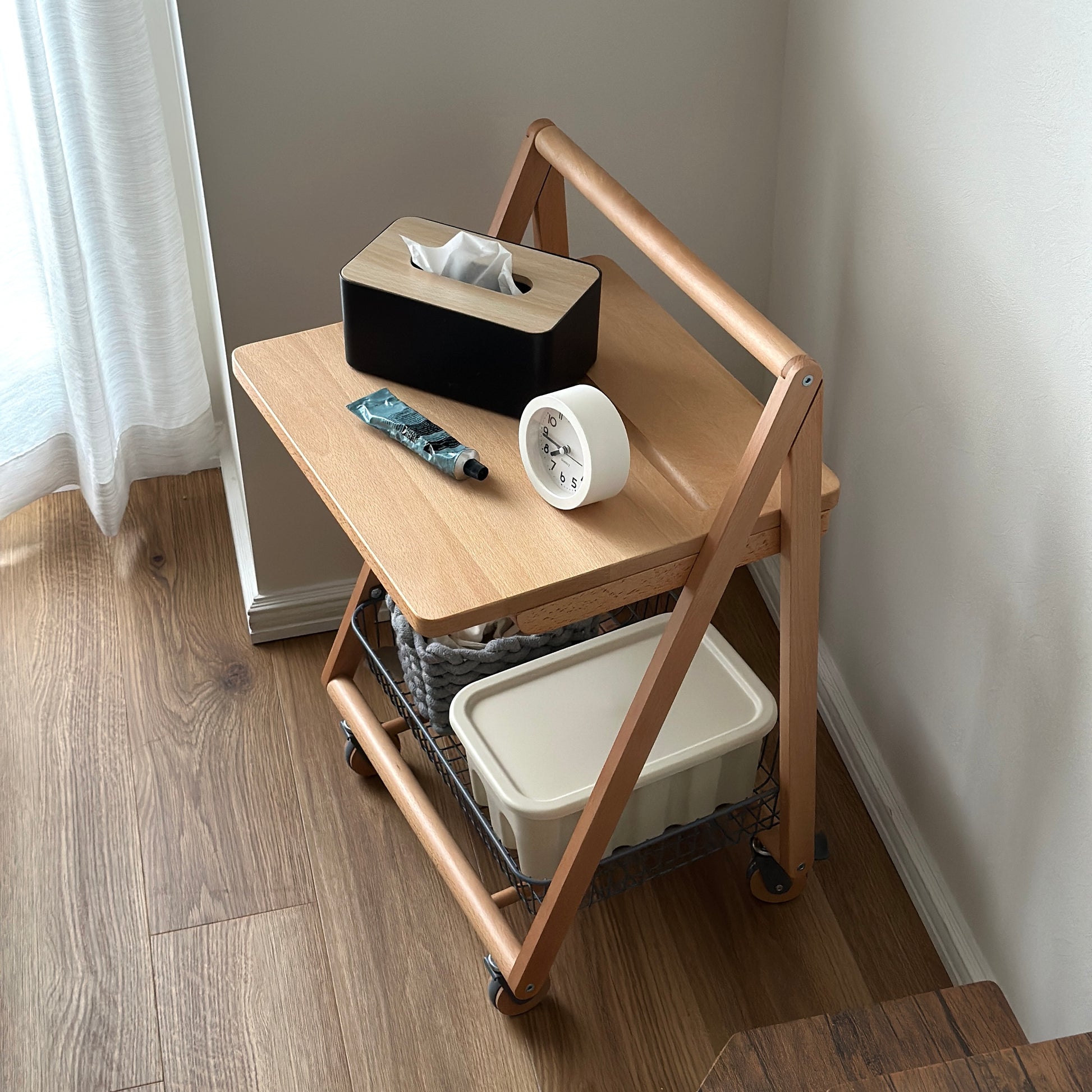 ナチュラルウッドのキャスター付きサイドテーブルにティッシュケースと時計、ハンドクリームが置かれている様子