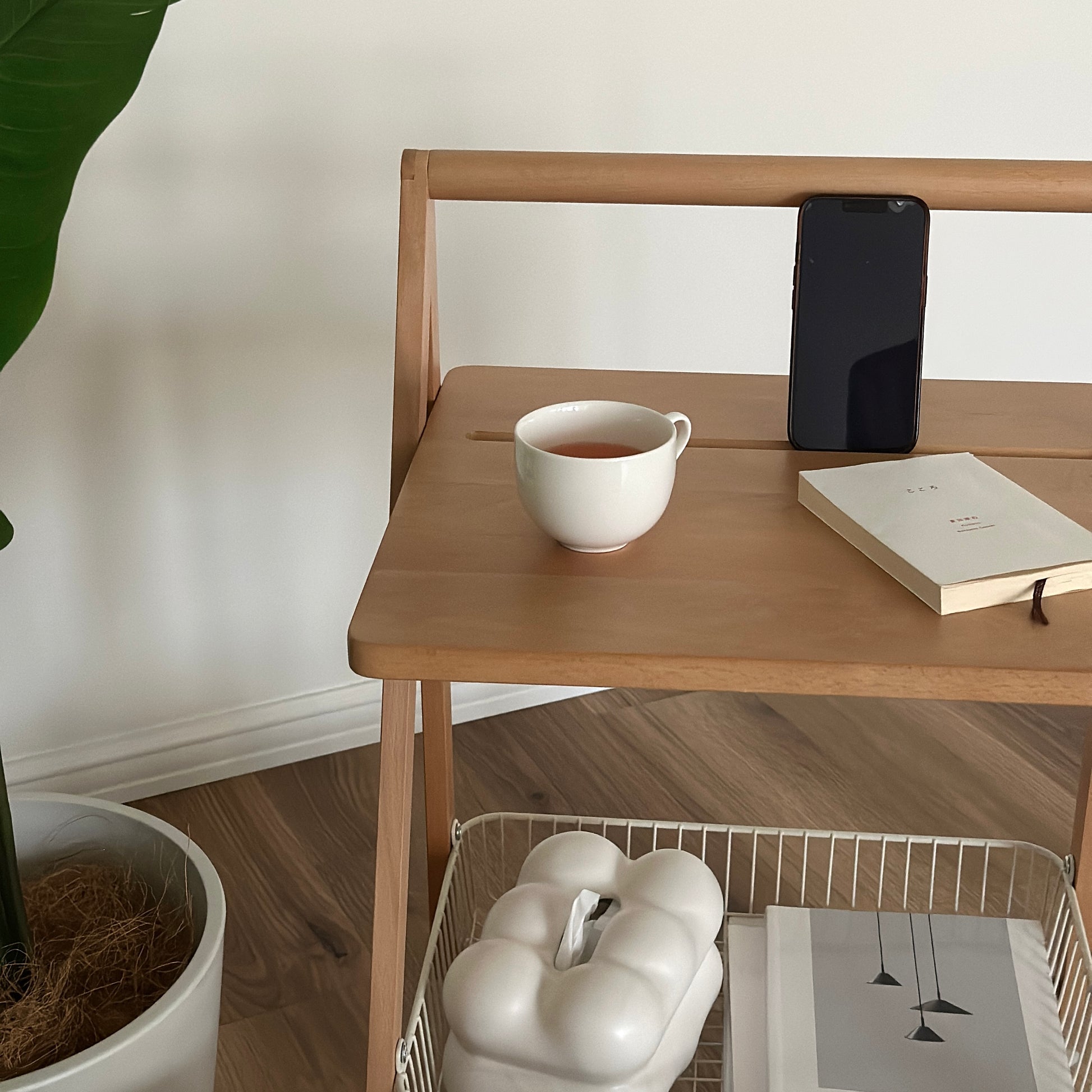 ナチュラルウッドのキャスター付きサイドテーブルの上にティーカップと文庫本、スマホが置かれてある