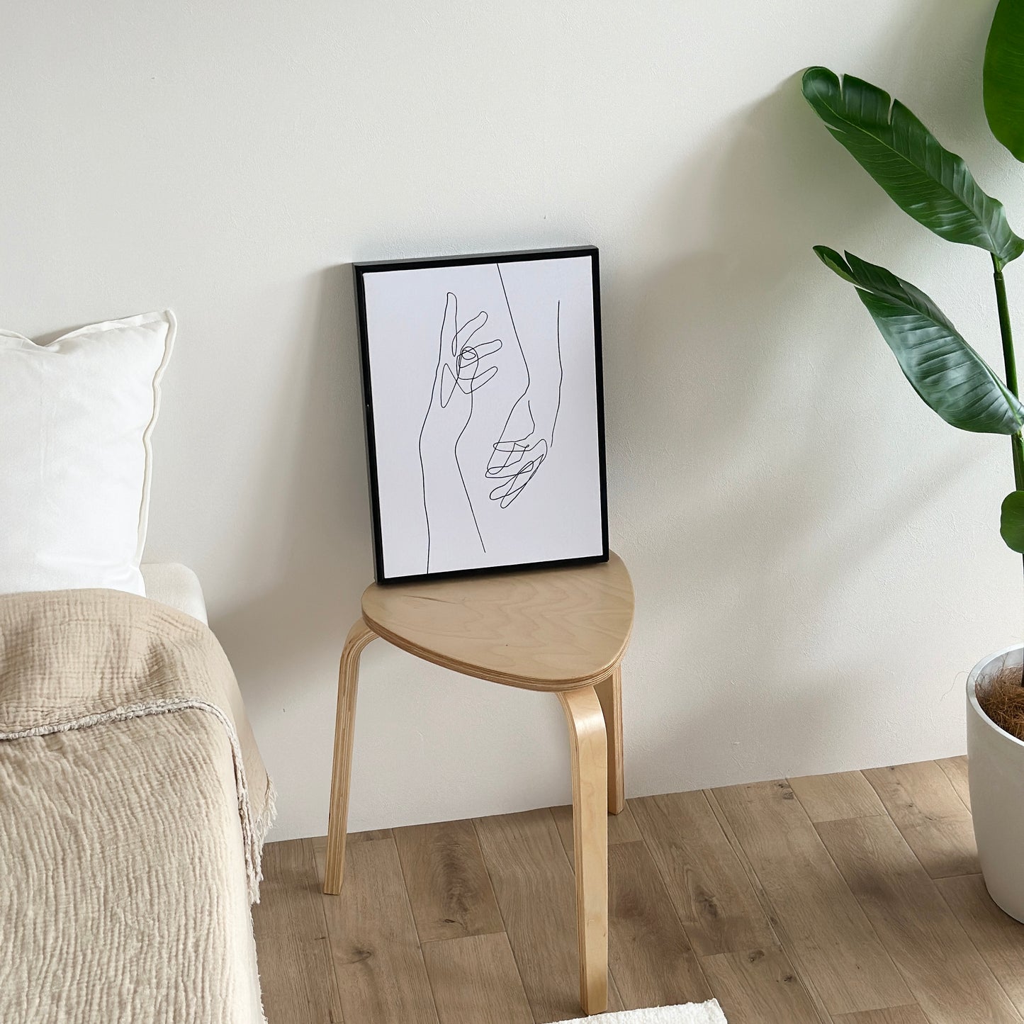 ベッド横に置かれたスツールの上に2つの手が描かれたアートが立てかけられている